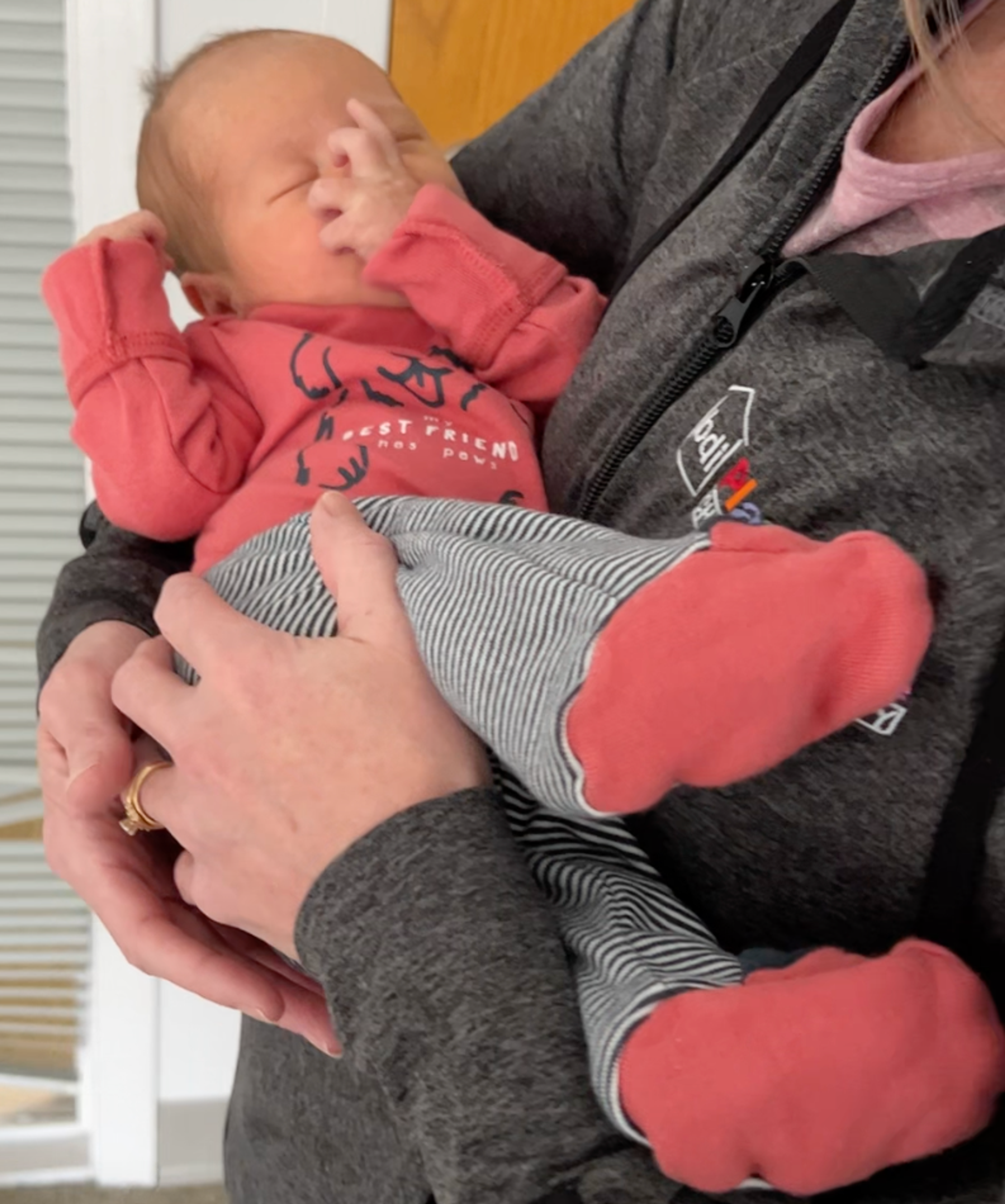 A team member in a gray BDI Playhouse jacket cradles a sleepy newborn dressed in red