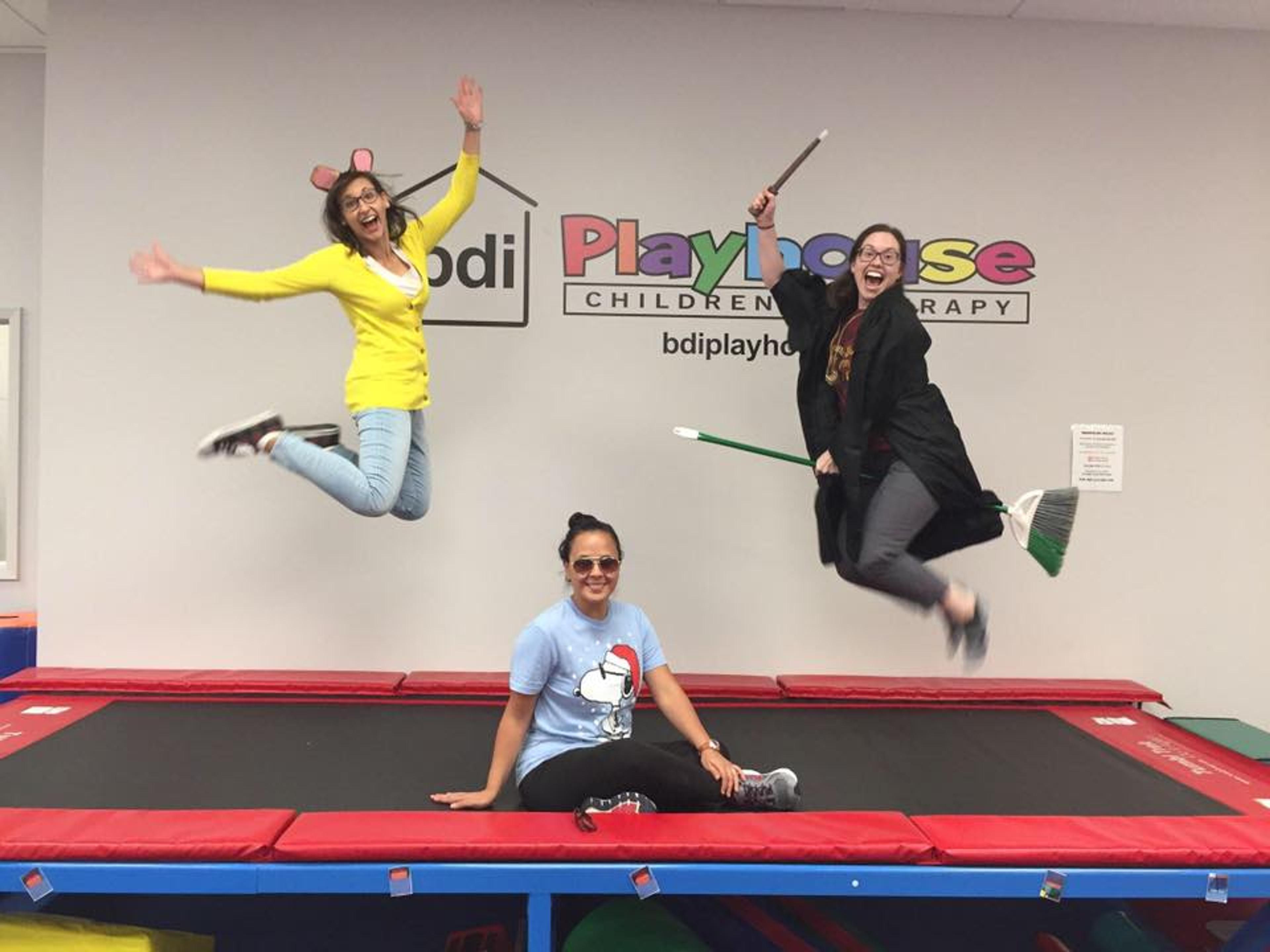 Two costumed staff members leap in the air beside a trampoline while a third sits on it, in front of the BDI Playhouse sign