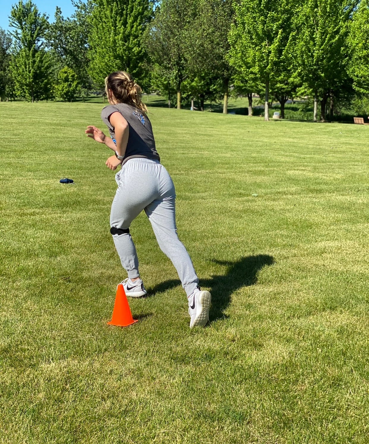 A teen athlete wearing a knee strap pushes off to sprint past an orange cone on a grass field
