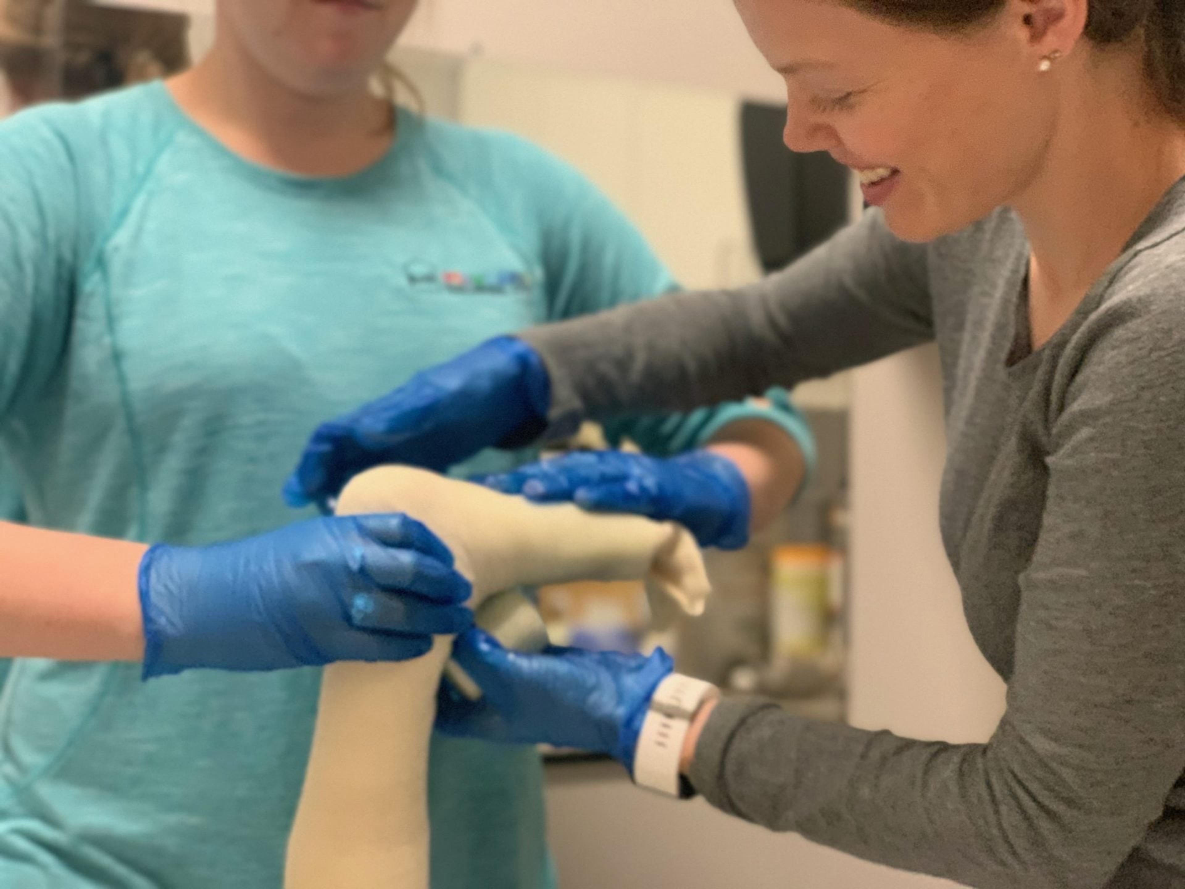 Two therapists in blue gloves wrap a soft cast around a child's foot and lower leg