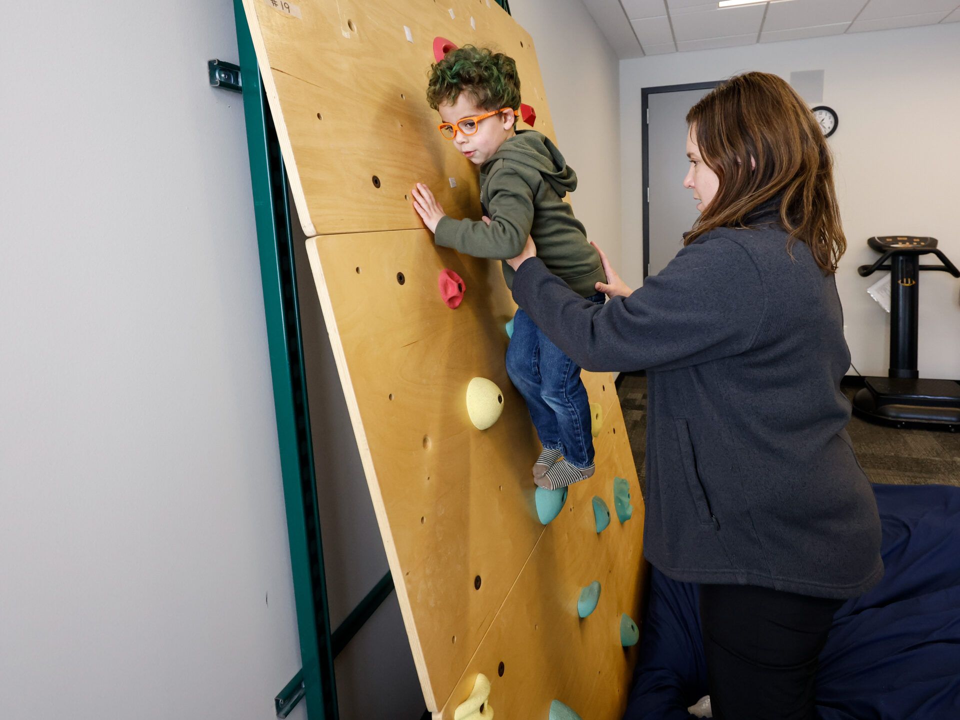 A child on the climbing wall with a therapist spotting