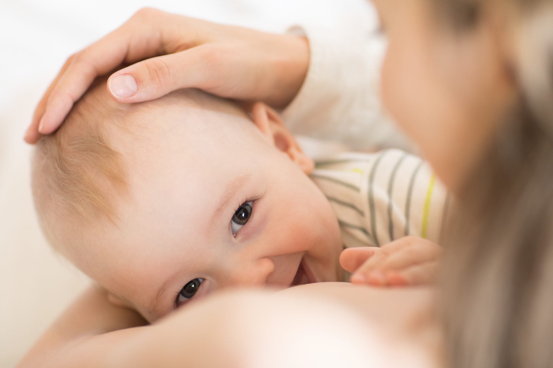 A baby looks up and smiles while nursing as the mother cradles the baby's head