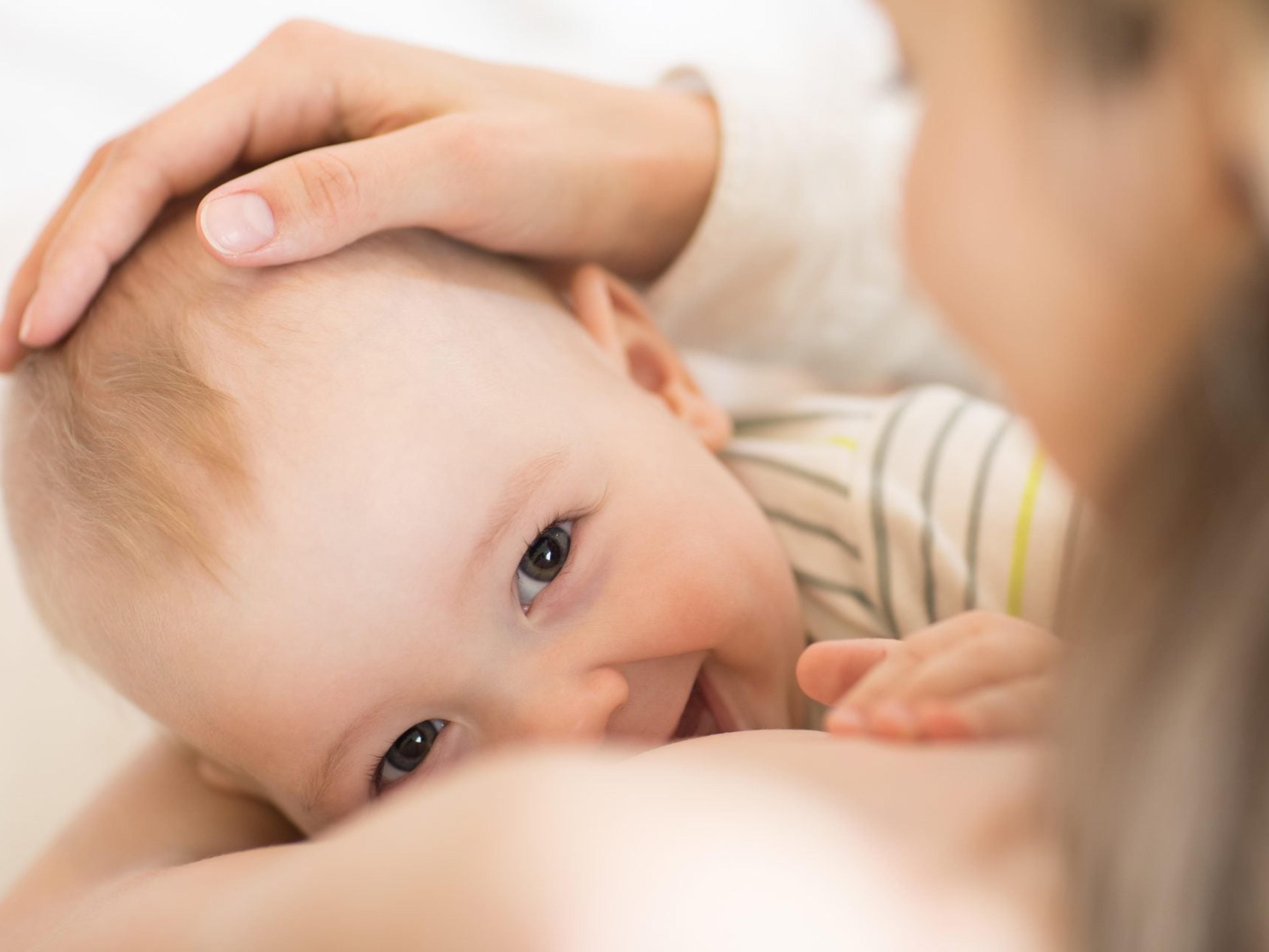 A baby looks up and smiles while nursing as the mother cradles the baby's head