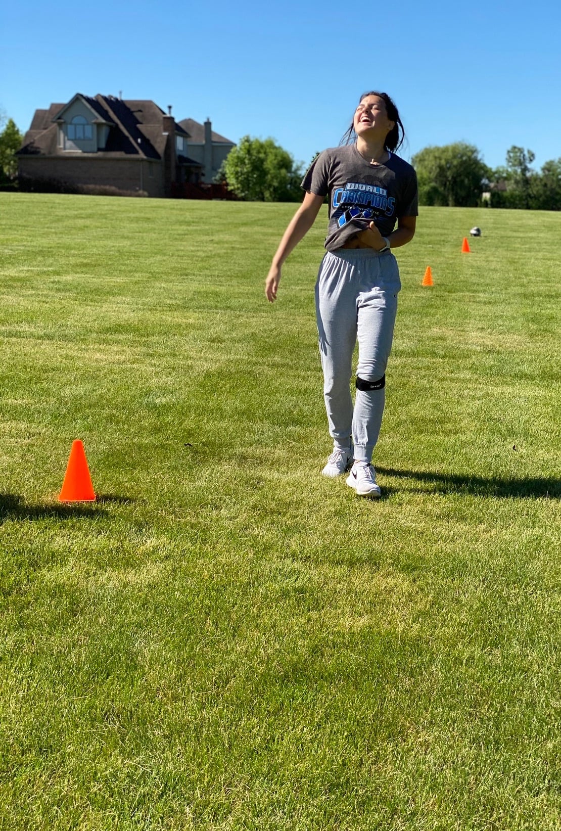 A smiling teen athlete wearing knee straps steps between orange cones on a grass field