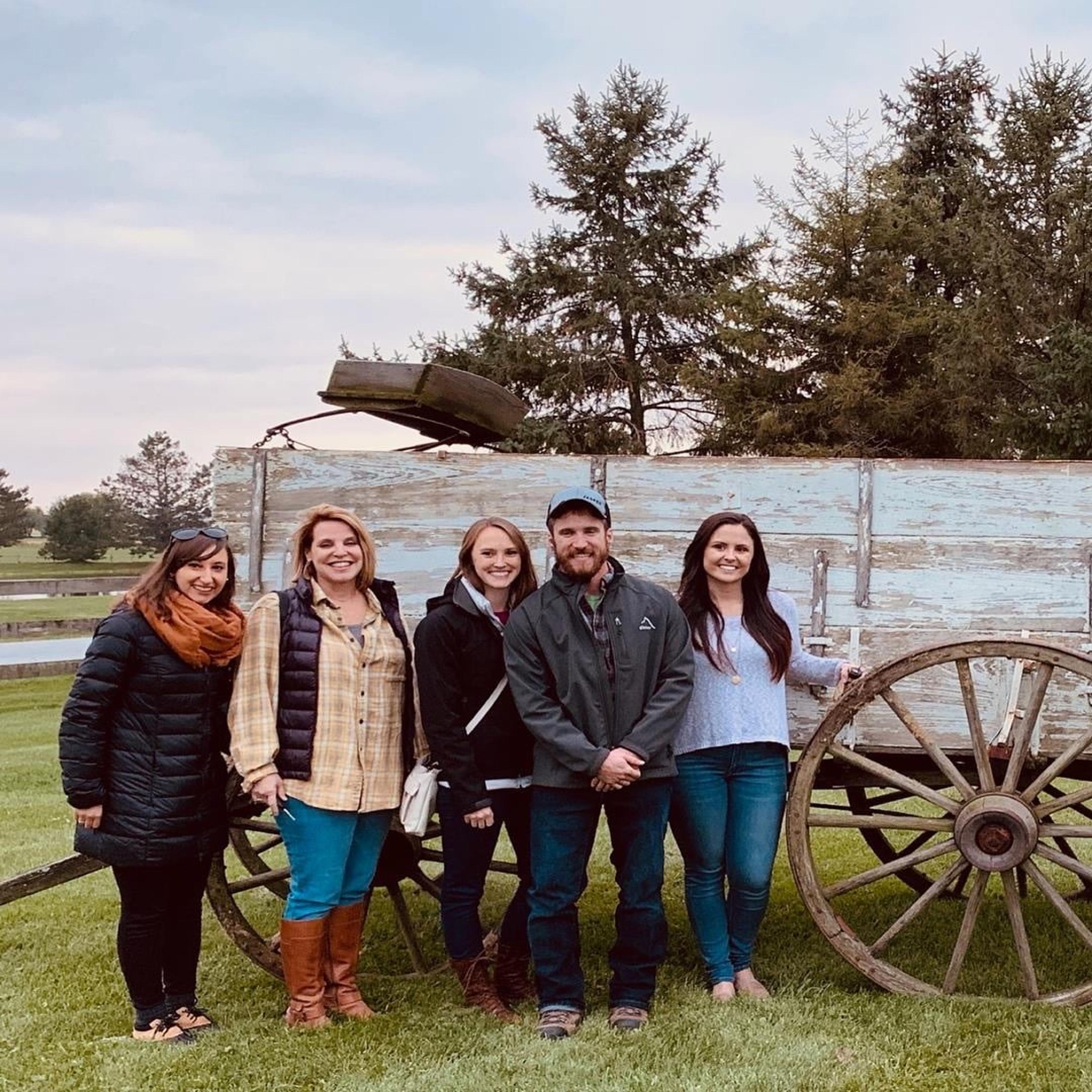 Five staff members pose in front of an old wooden wagon during a farm outing