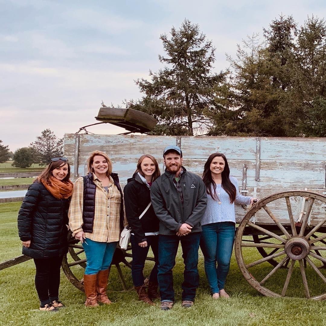 Five staff members pose in front of an old wooden wagon during a farm outing