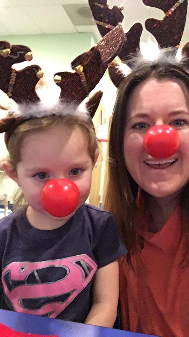 A woman and a toddler wearing reindeer antlers and red clown noses smile for a holiday selfie