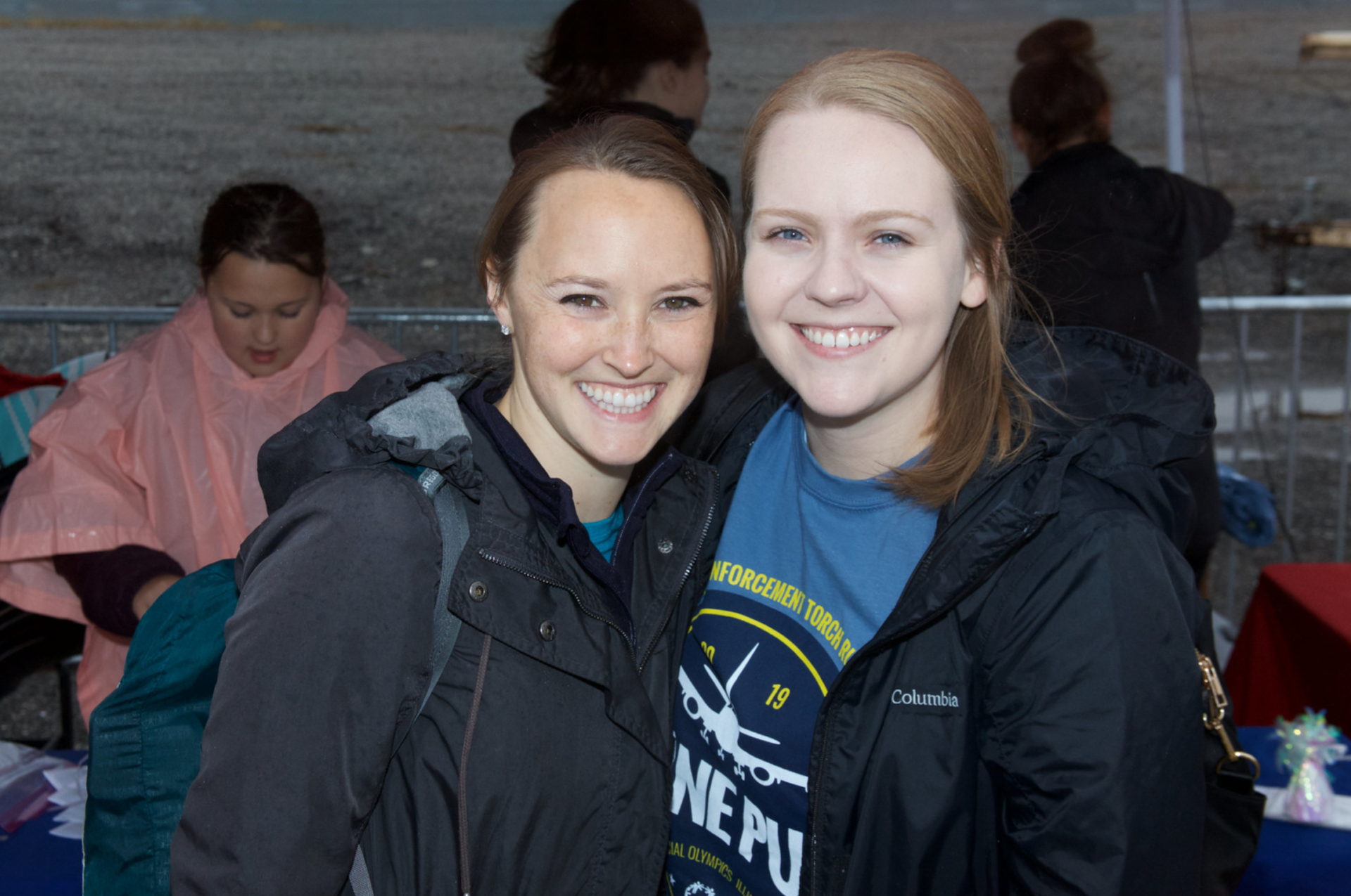 Two smiling staff members in rain jackets pose together at the outdoor Plane Pull event