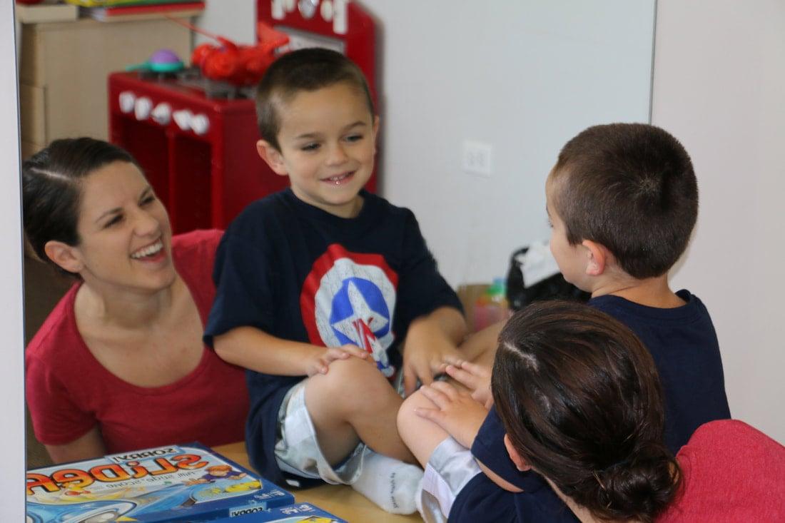 A therapist sits on the floor smiling with three young children during a group activity