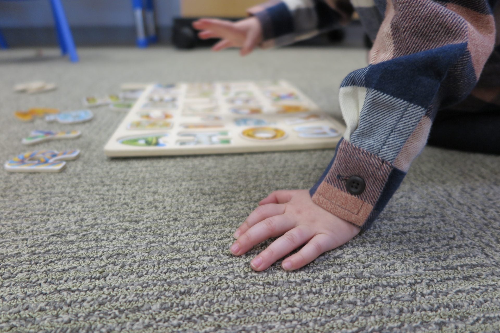 Close-up of a child's hand planted on the carpet while reaching toward a wooden alphabet puzzle