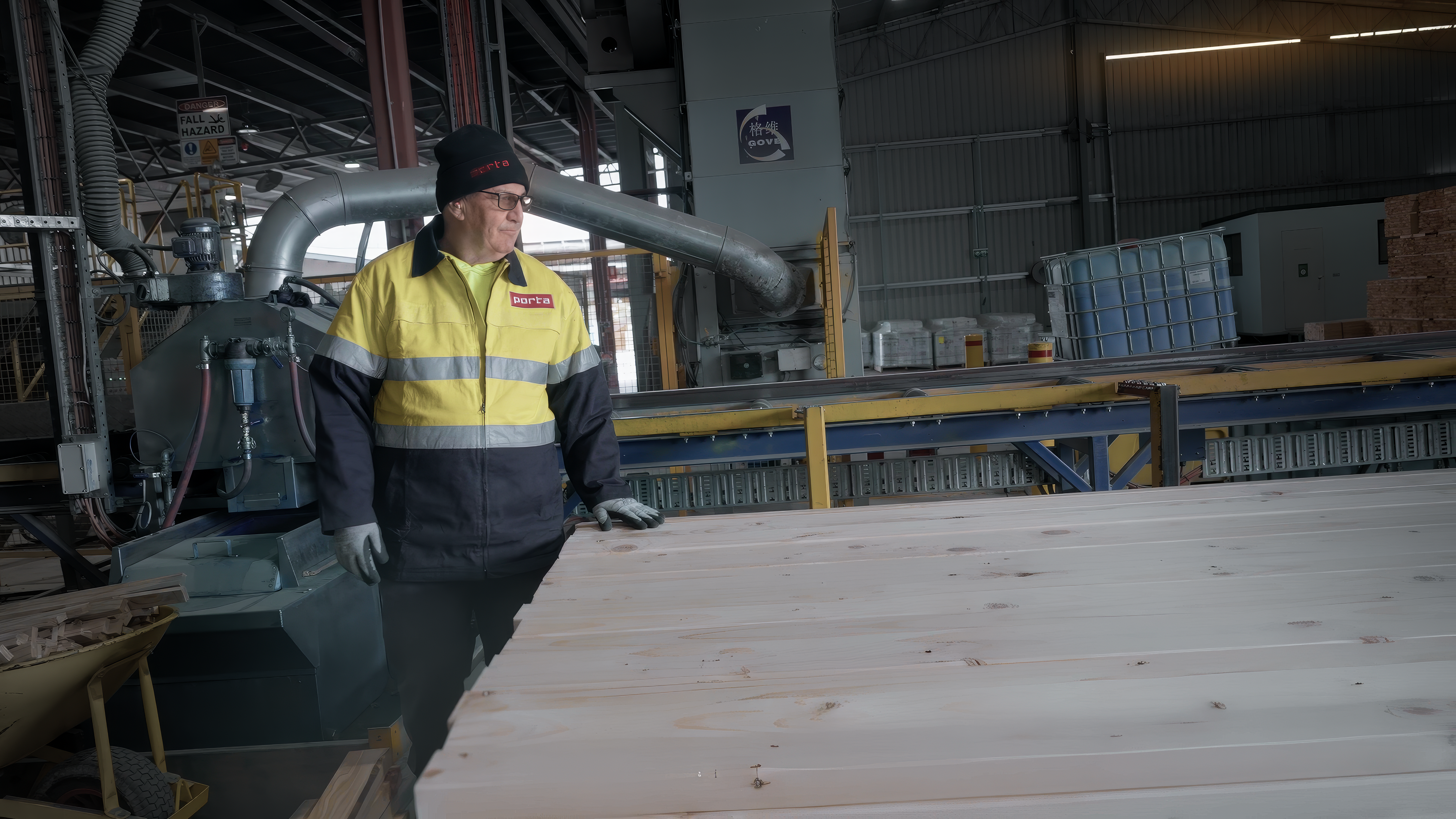 A Porta worker in uniform standing inside a factory next to stacked timbers.