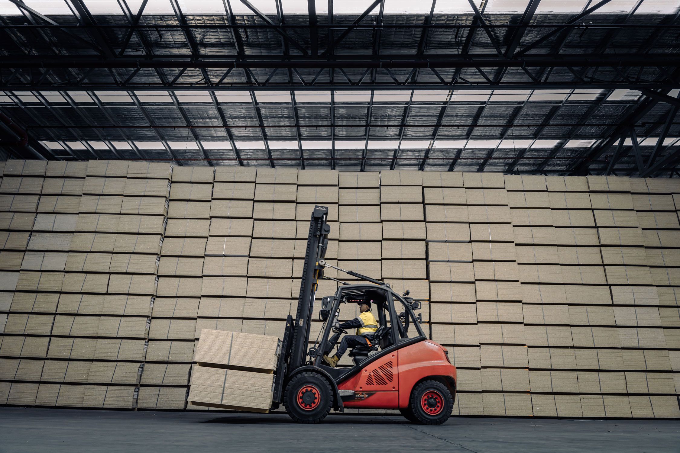 A forklift carrying a pack of particle boards in front of stacks of packs of particle board