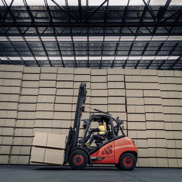 A forklift carrying a pack of particle boards in front of stacks of packs of particle board