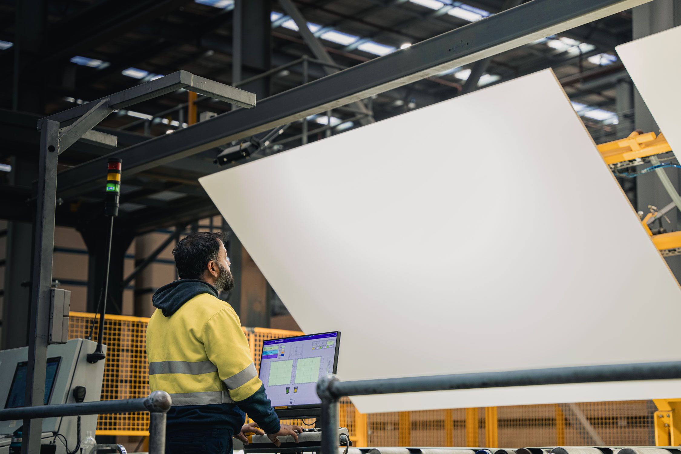 A worker standing in front of a computer checking a large panel of white board