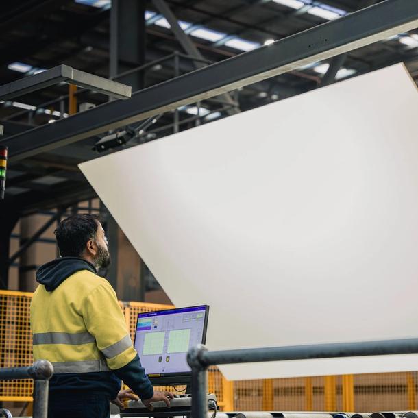 A worker standing in front of a computer checking a large panel of white board