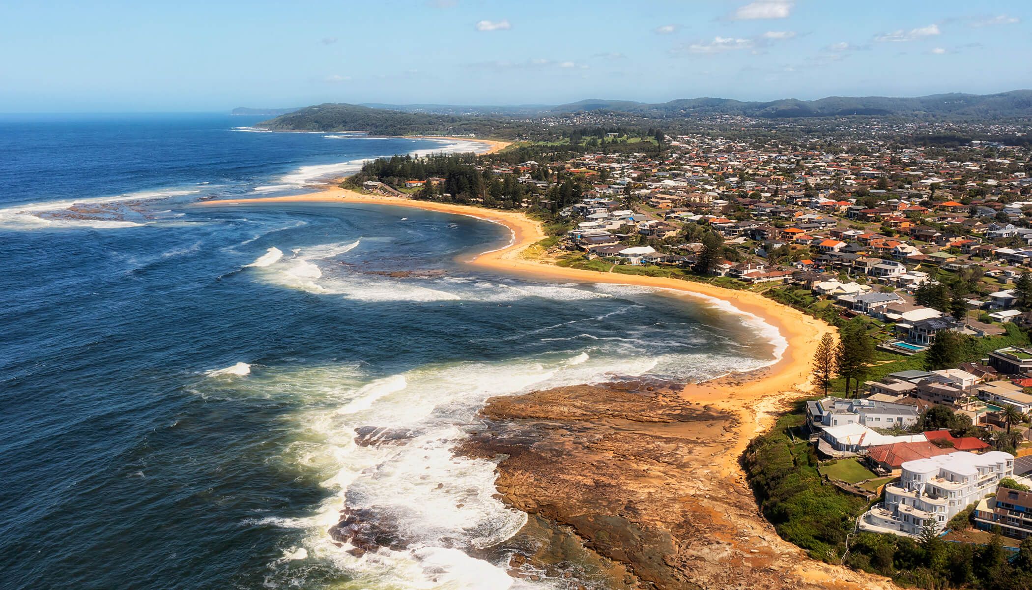 Aerial view of a beach with ocean waves and houses along the shore.