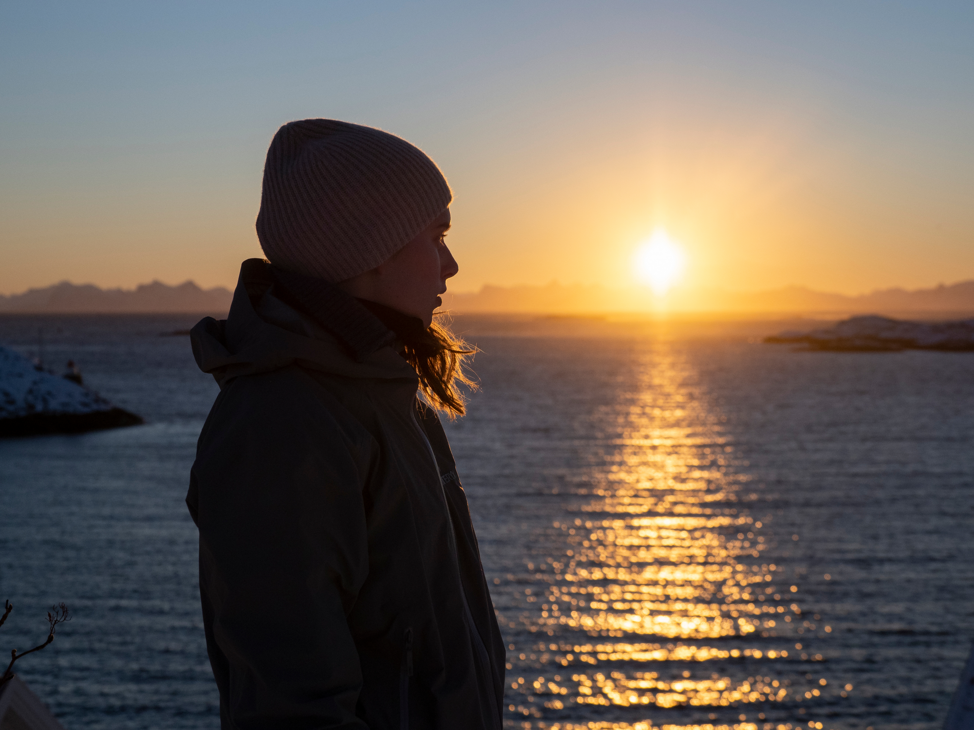 Ung kvinne ser mot venstre med solnedgang og havet som bakgrunn
