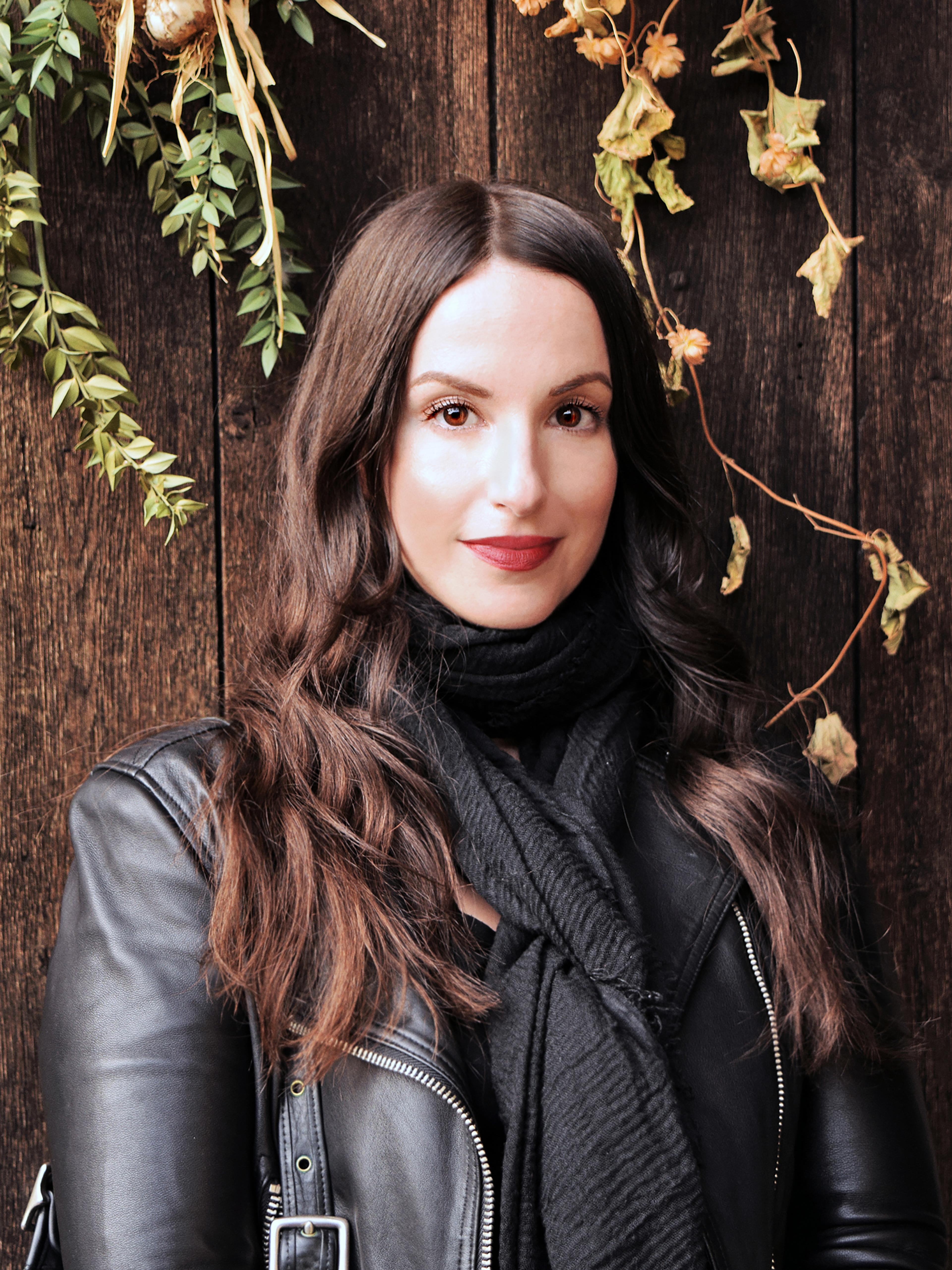 A woman with long brown hair stands in front of a wooden fence
