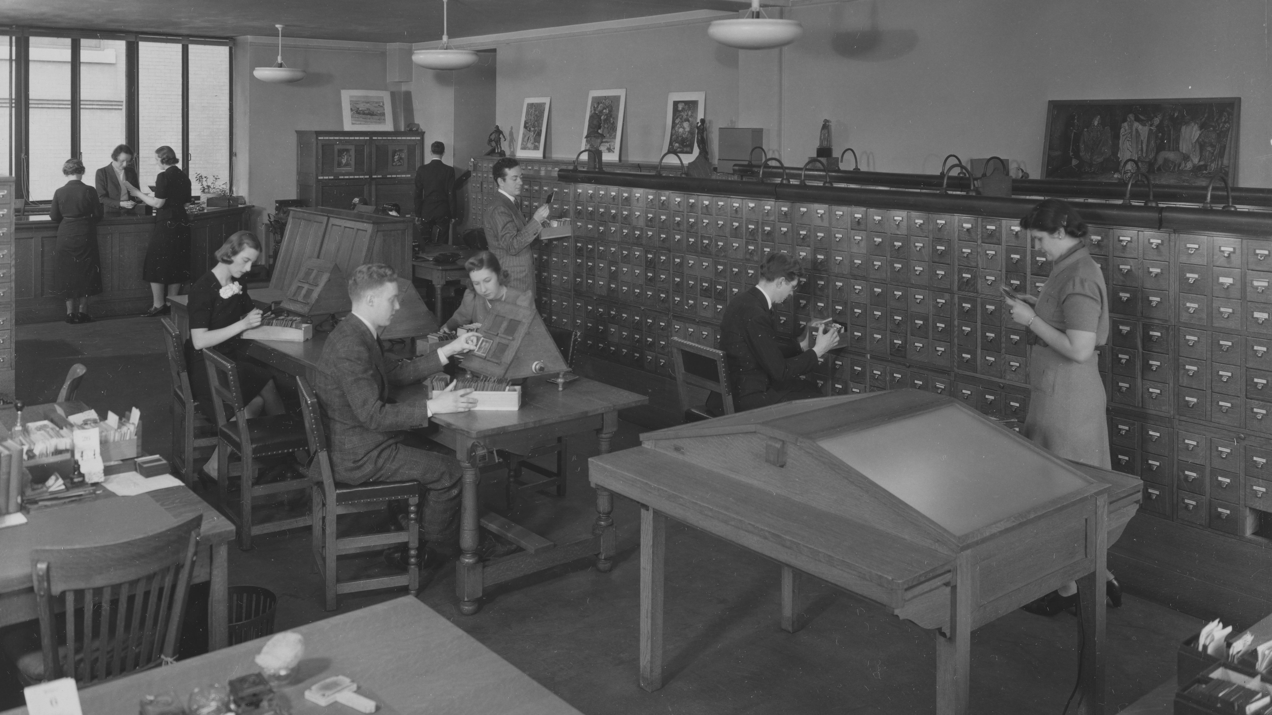 A black and white photograph depicting a group of workers examining lantern slides in the Met's Photograph and Extension Division