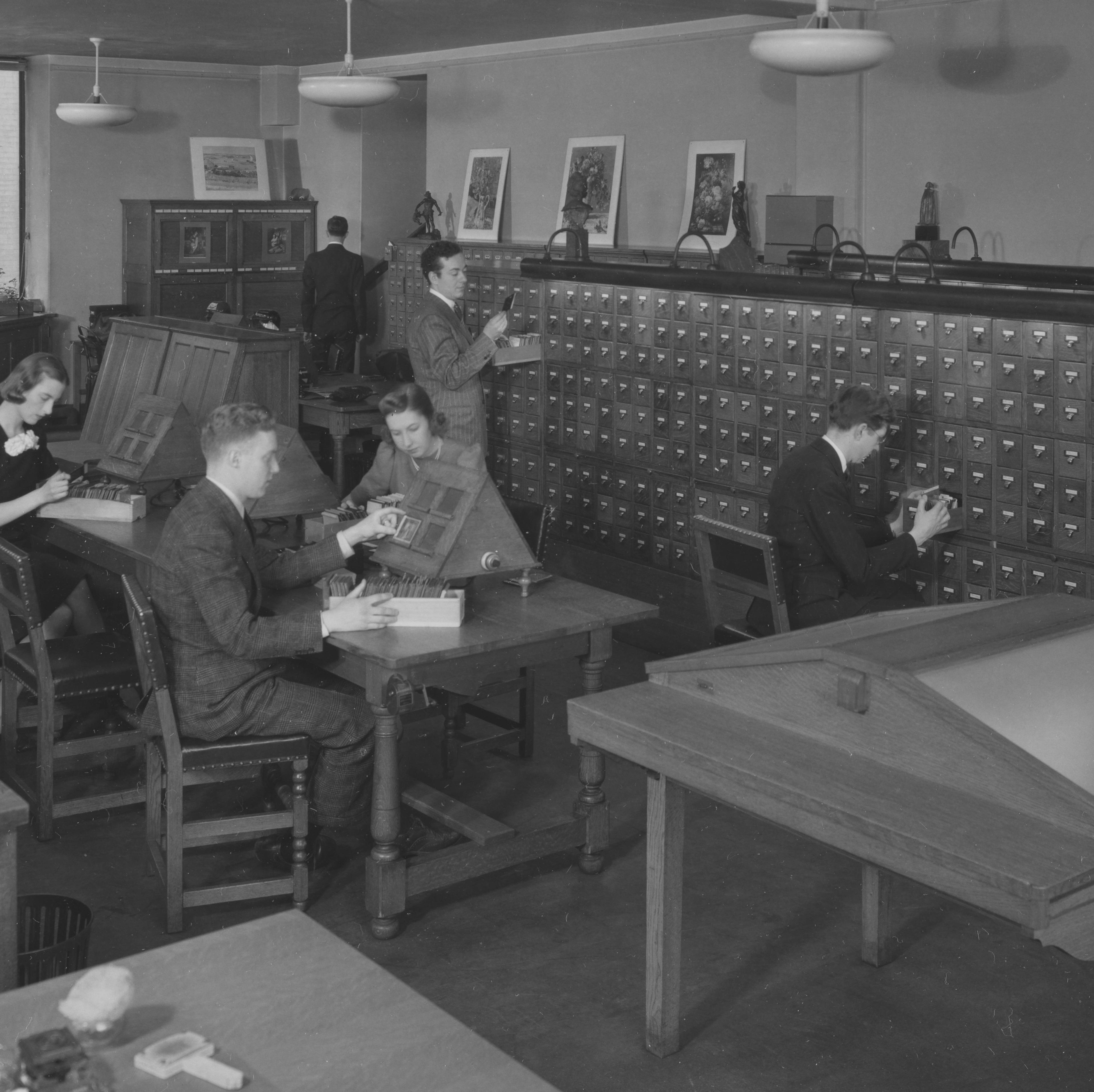 A black and white photograph depicting a group of workers examining lantern slides in the Met's Photograph and Extension Division