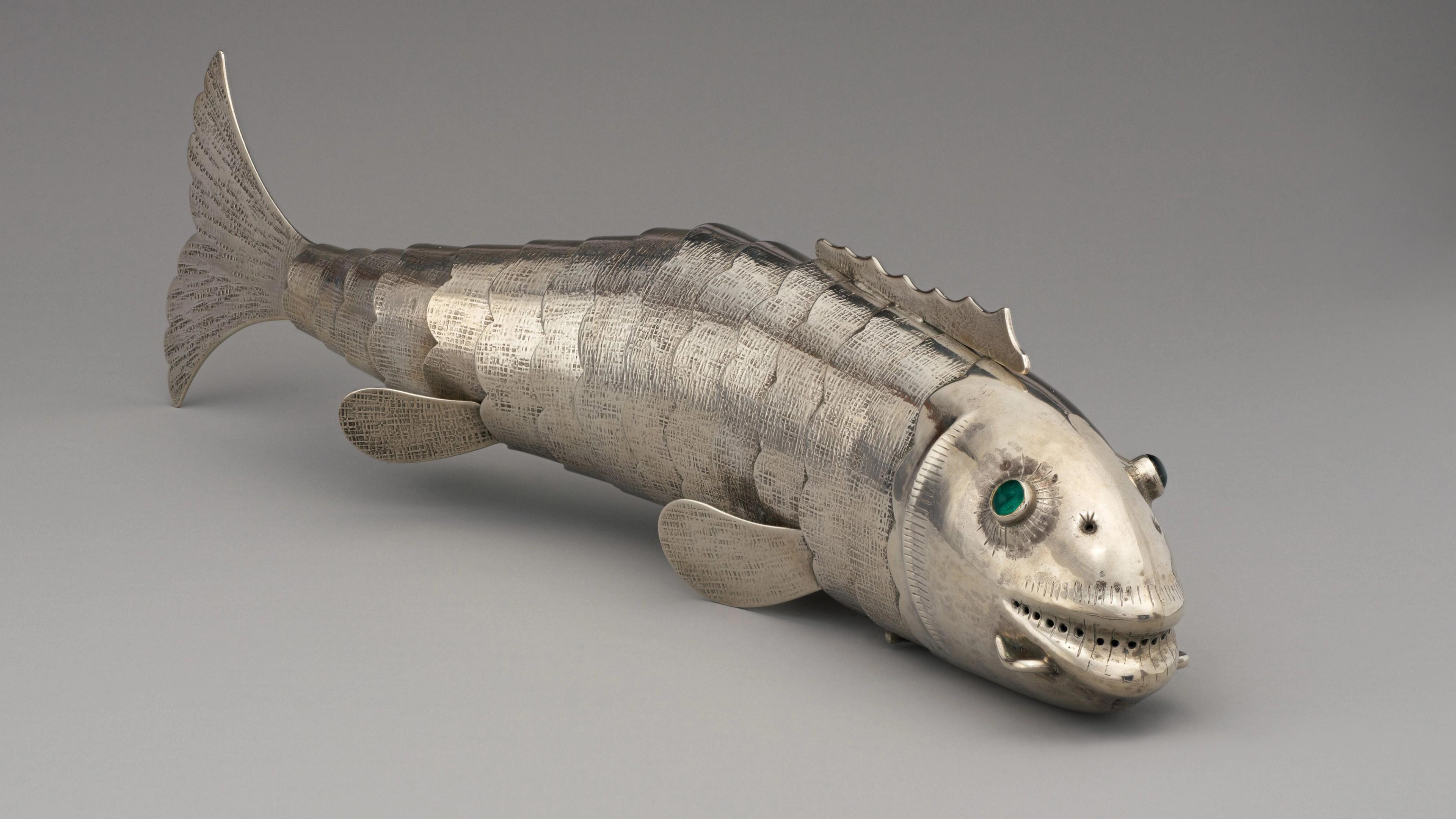 Silver fish sculpture with emerald green eyes, lifelike scales, and visible details.