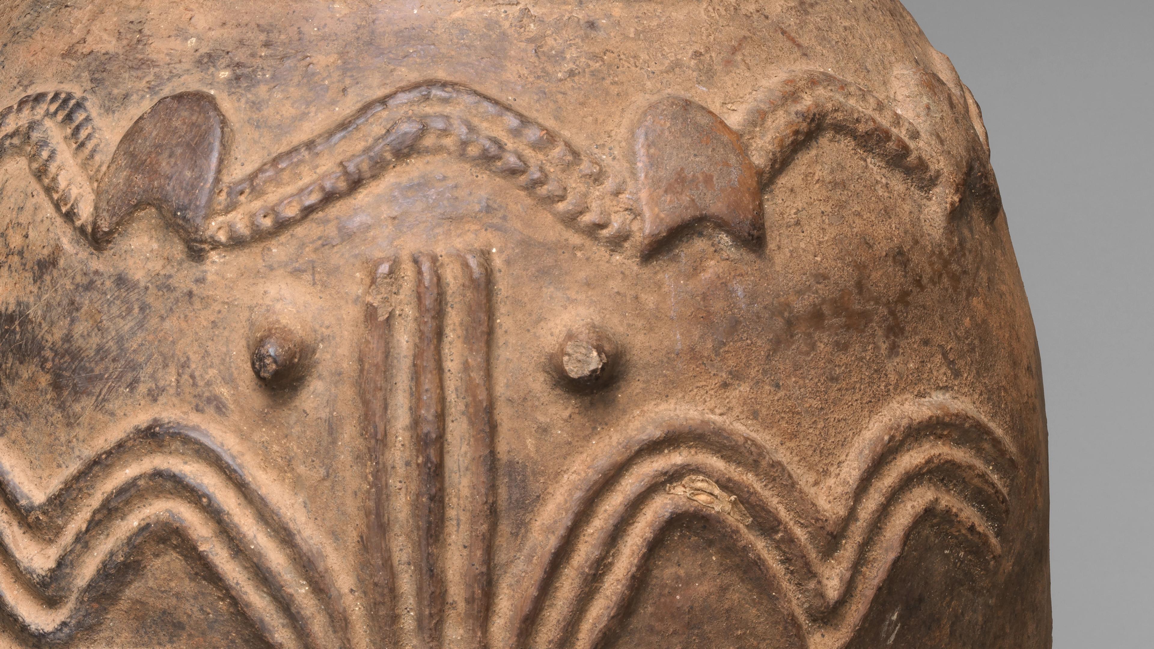 Detail of a brown ceramic vessel showing patterns of raised lines and circles.