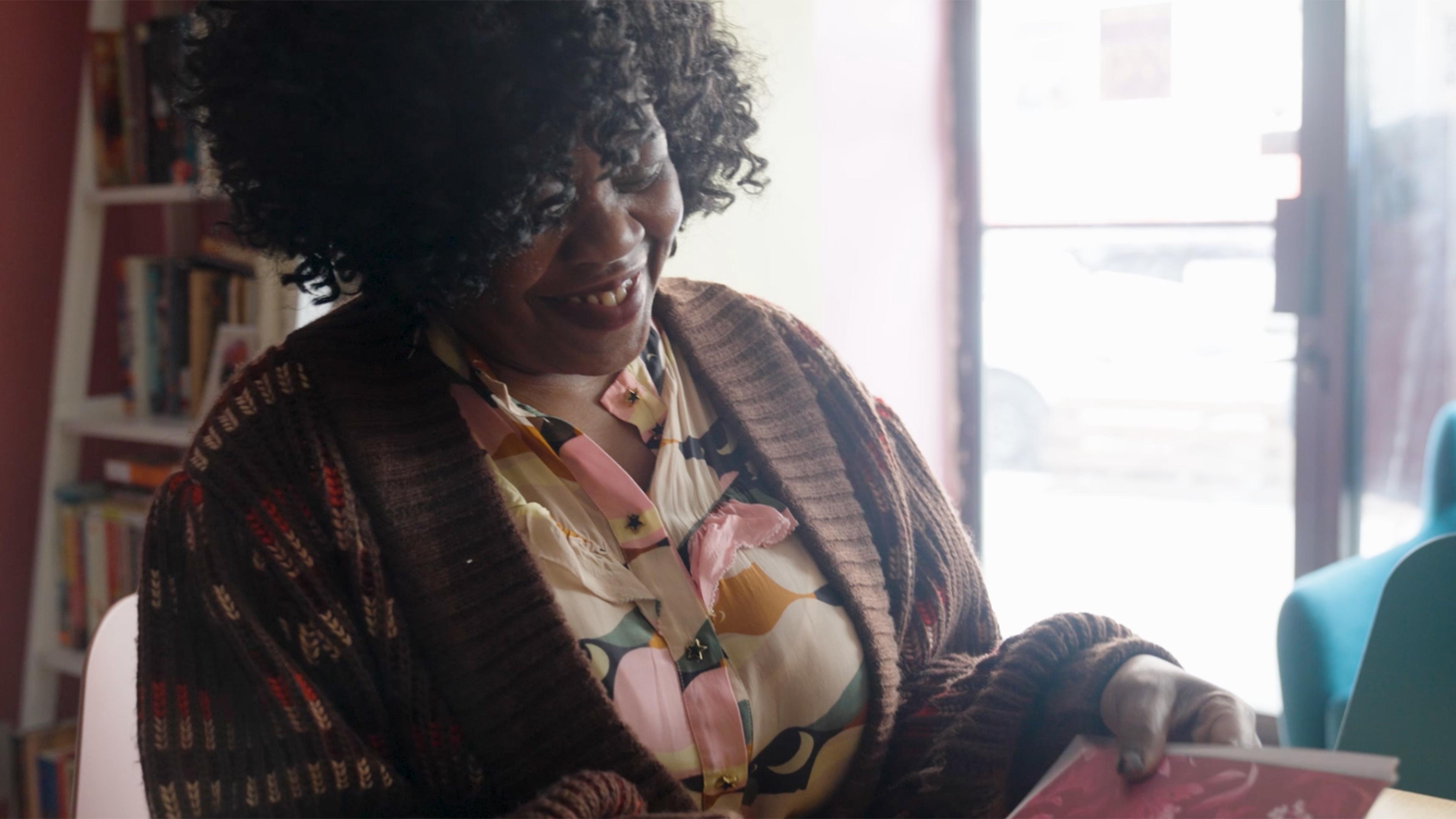 A smiling woman, her face turned downward towards an open book.