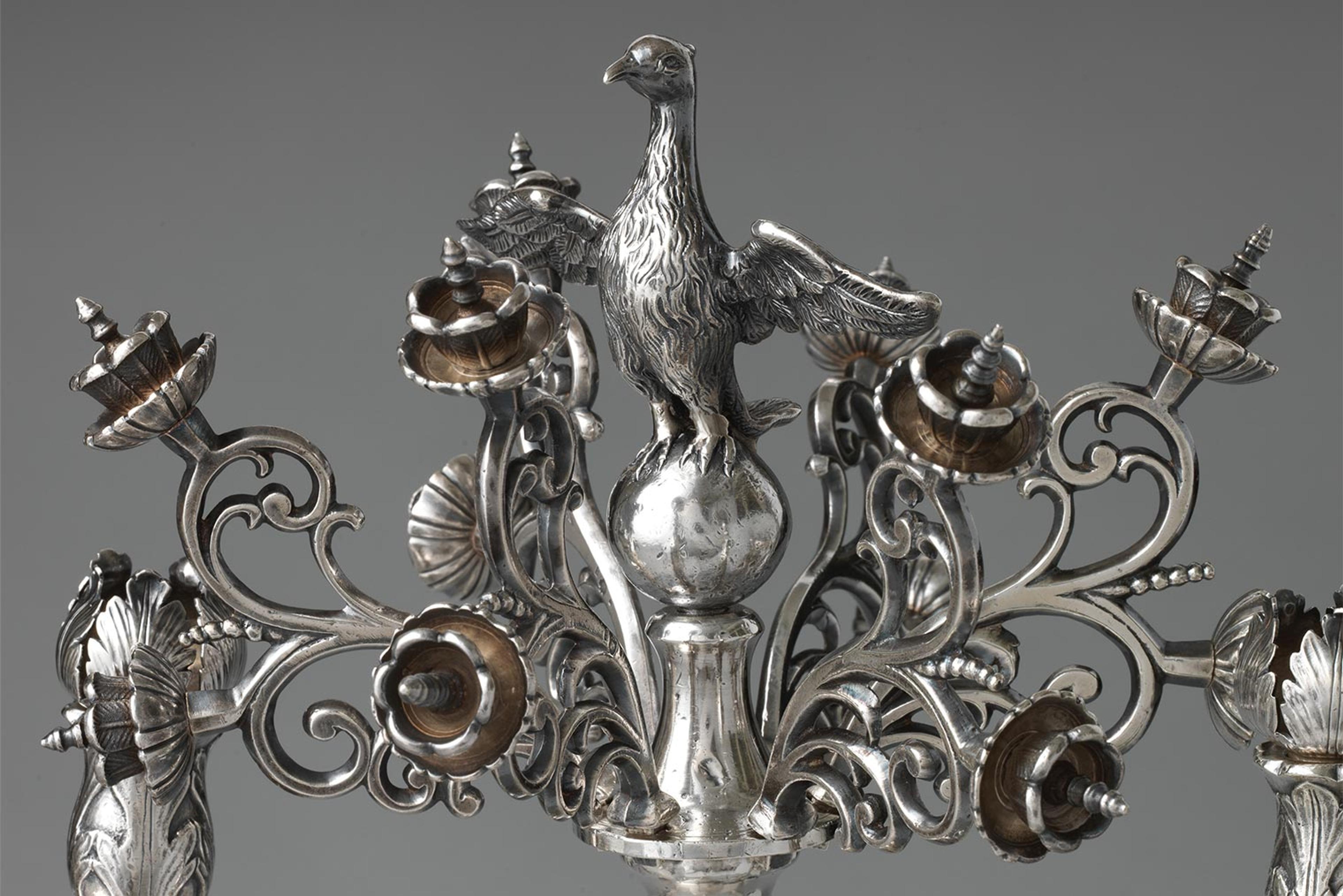 An ornate silver menorah with flowers, birds, and lions
