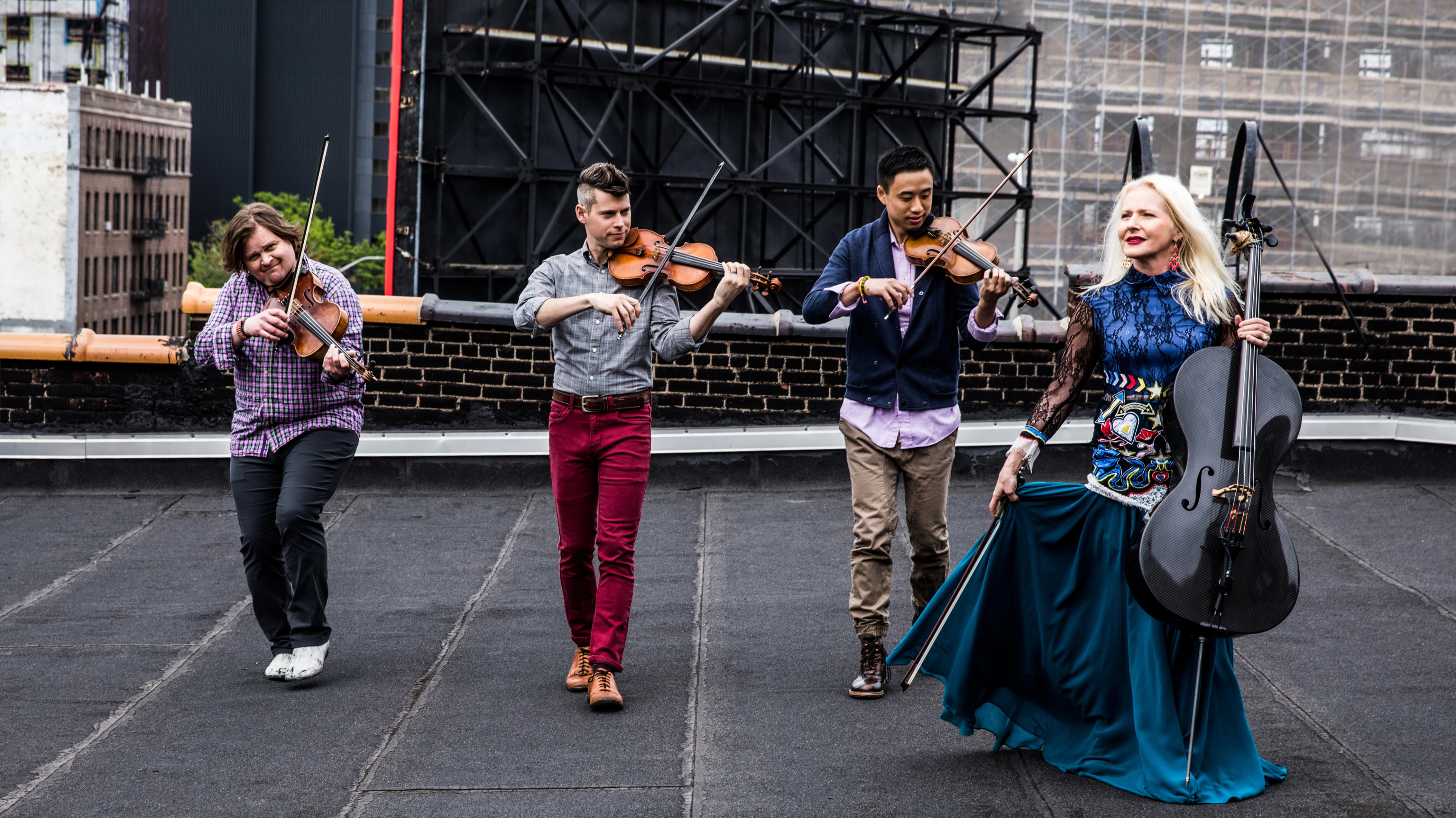 Four members of a string quartet hold their instruments and walk toward the camera.