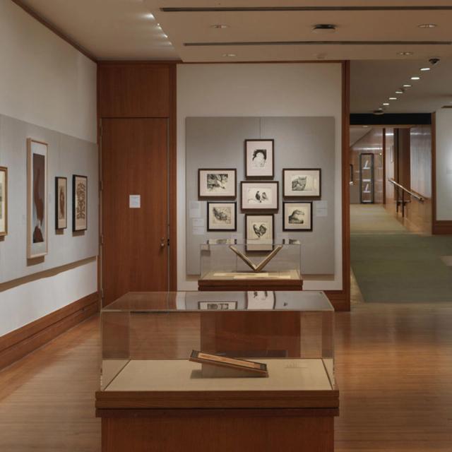 Room with wooden floors, gray walls, and framed drawings and prints.