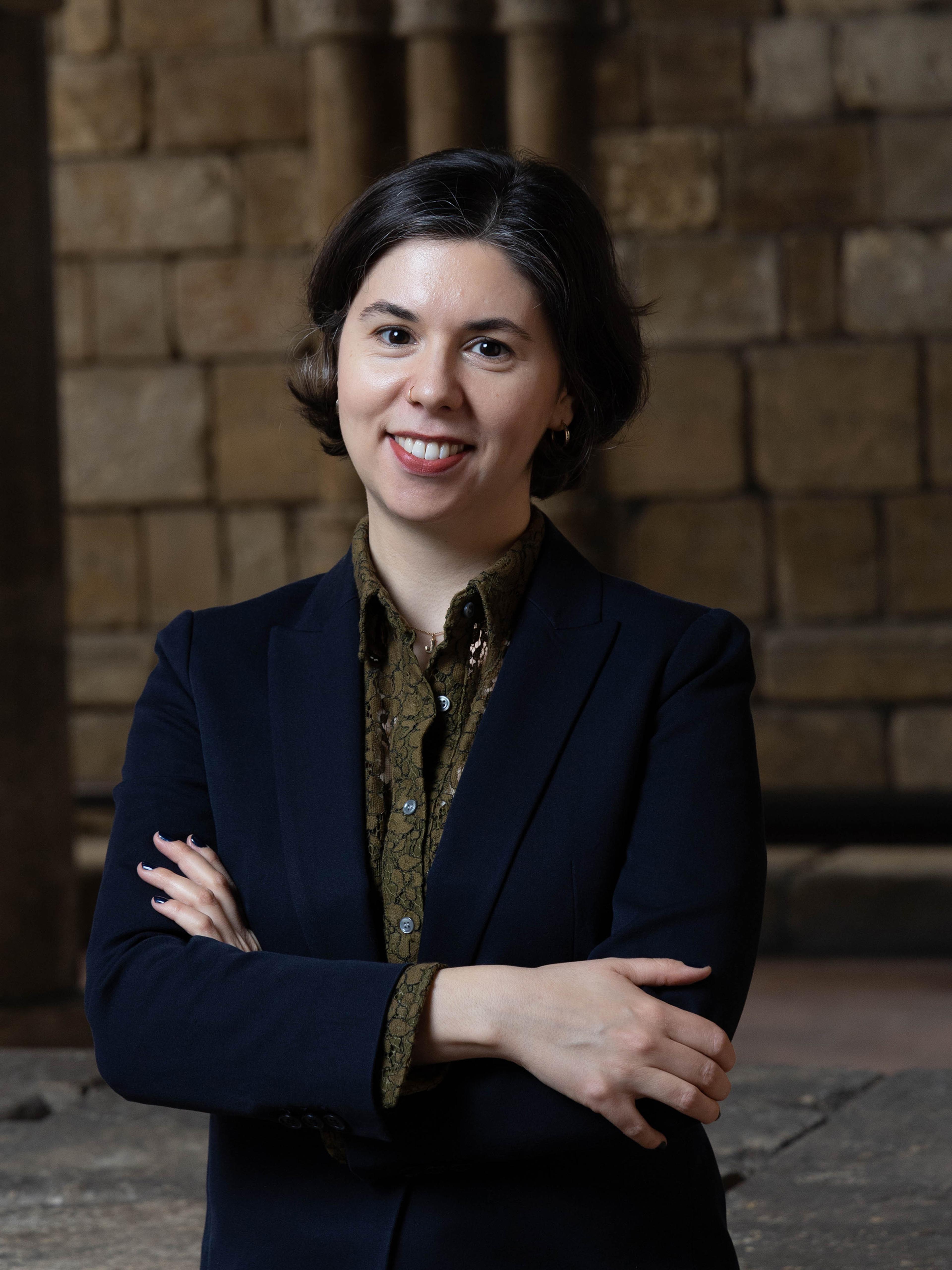 A woman wearing a navy blazer poses in front of a stone wall