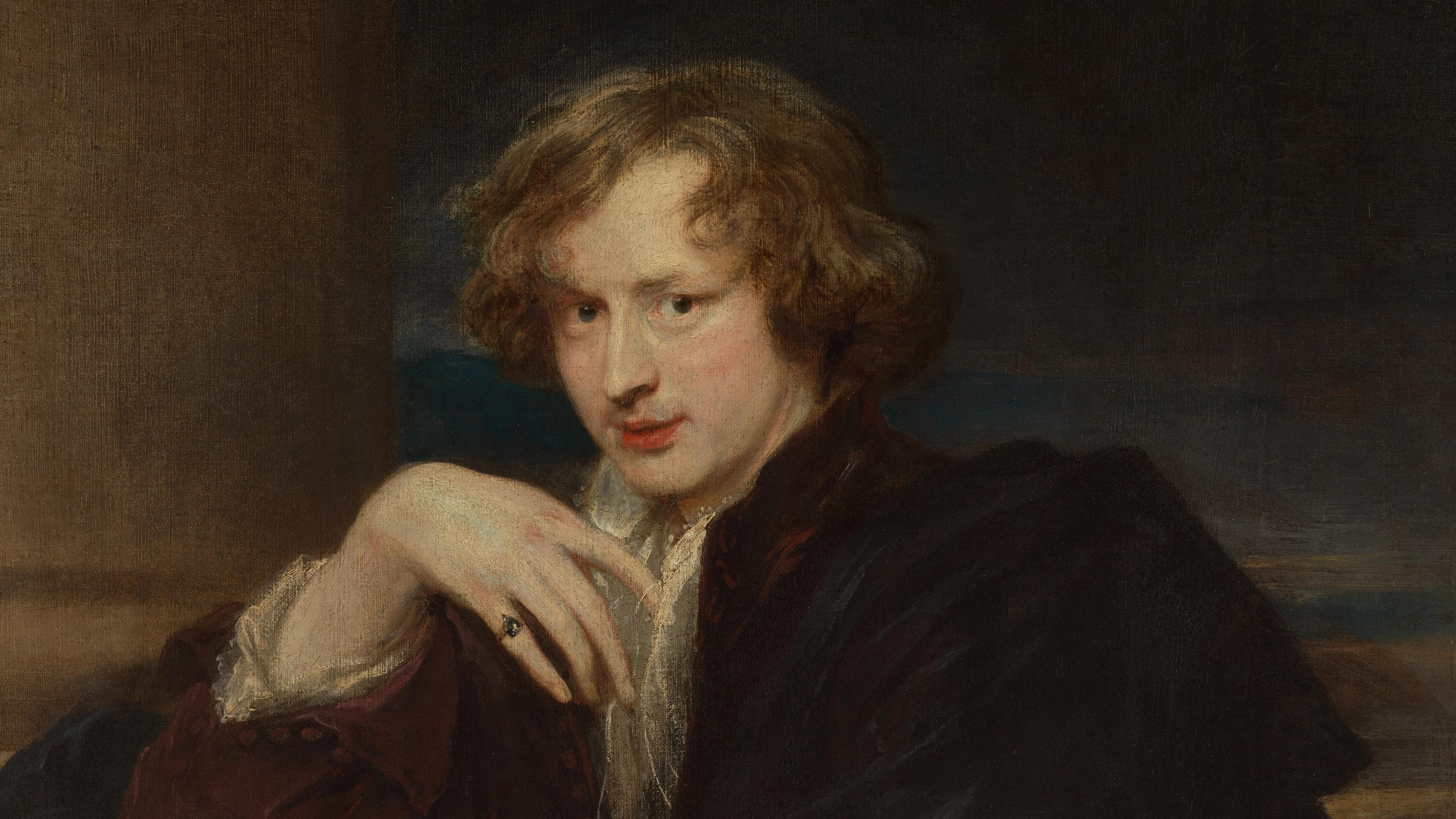 A young man with wavy hair stares at the viewer, his right hand angled delicately in front of his chest.