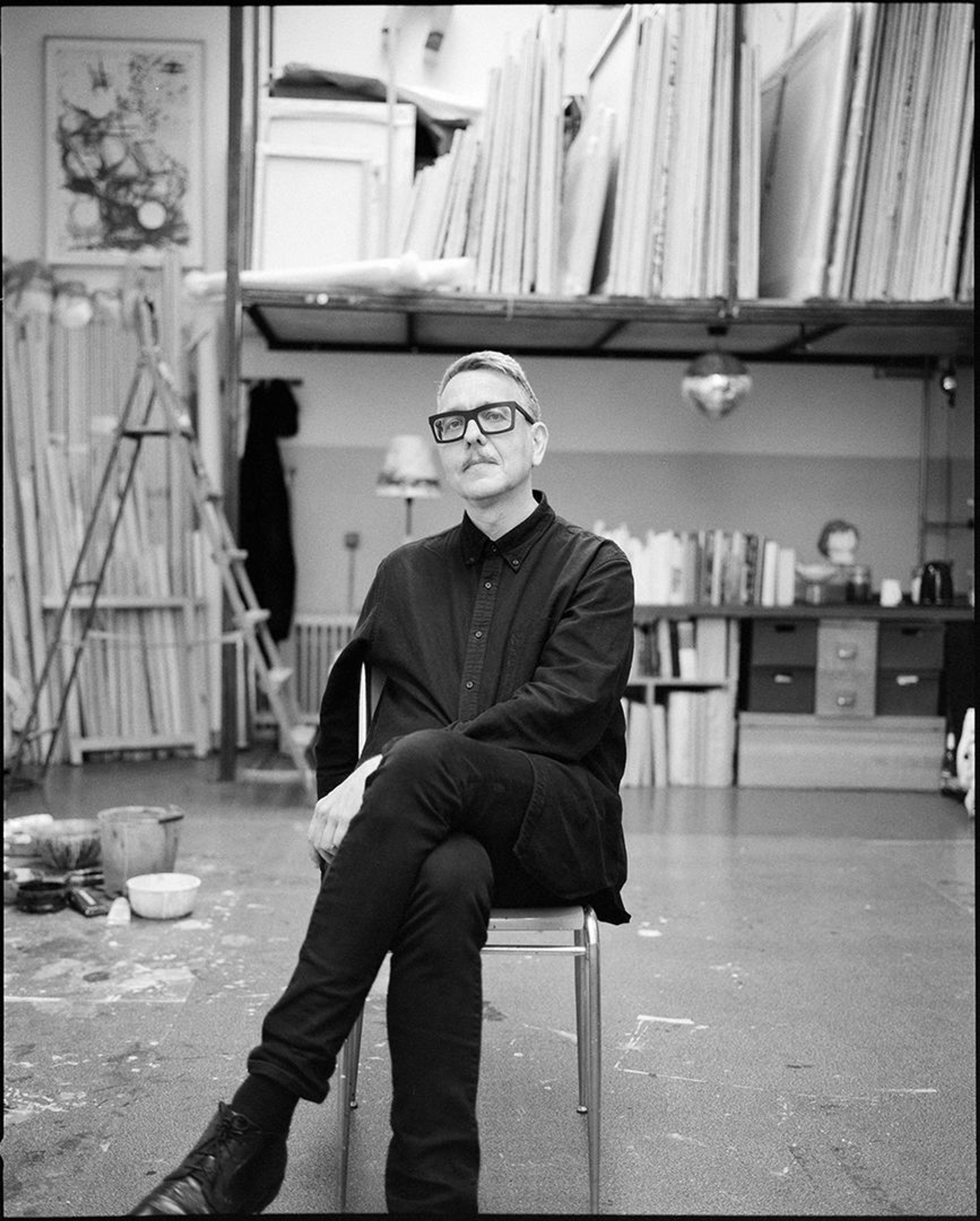 black and white photograph of a man wearing black seated in a studio