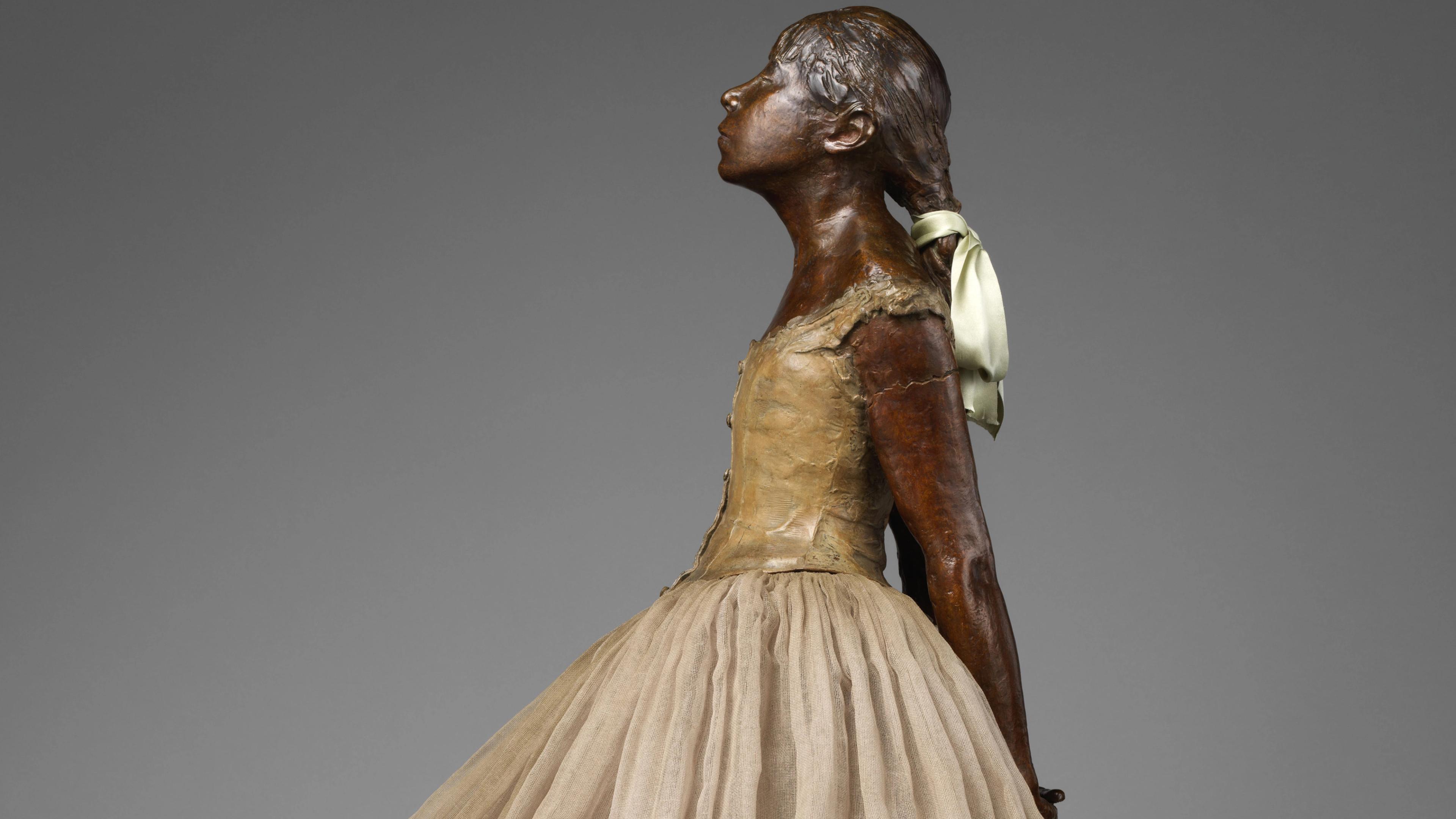Detail of a Degas bronze sculpture showing a young girl in a ballet dress gazing upward, her hair tied back with a satin ribbon.