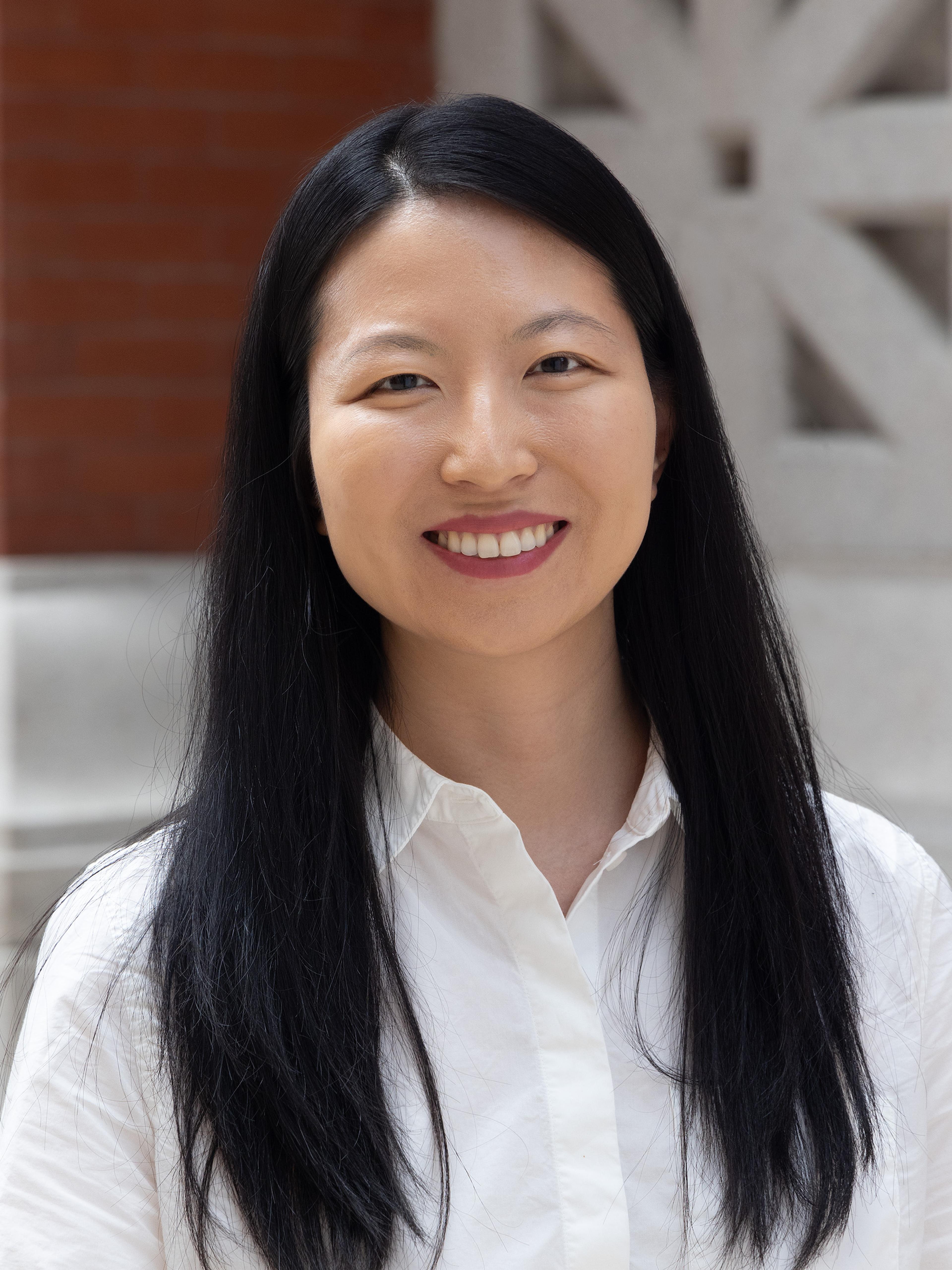 A woman with black hair smiles in front of a brick building