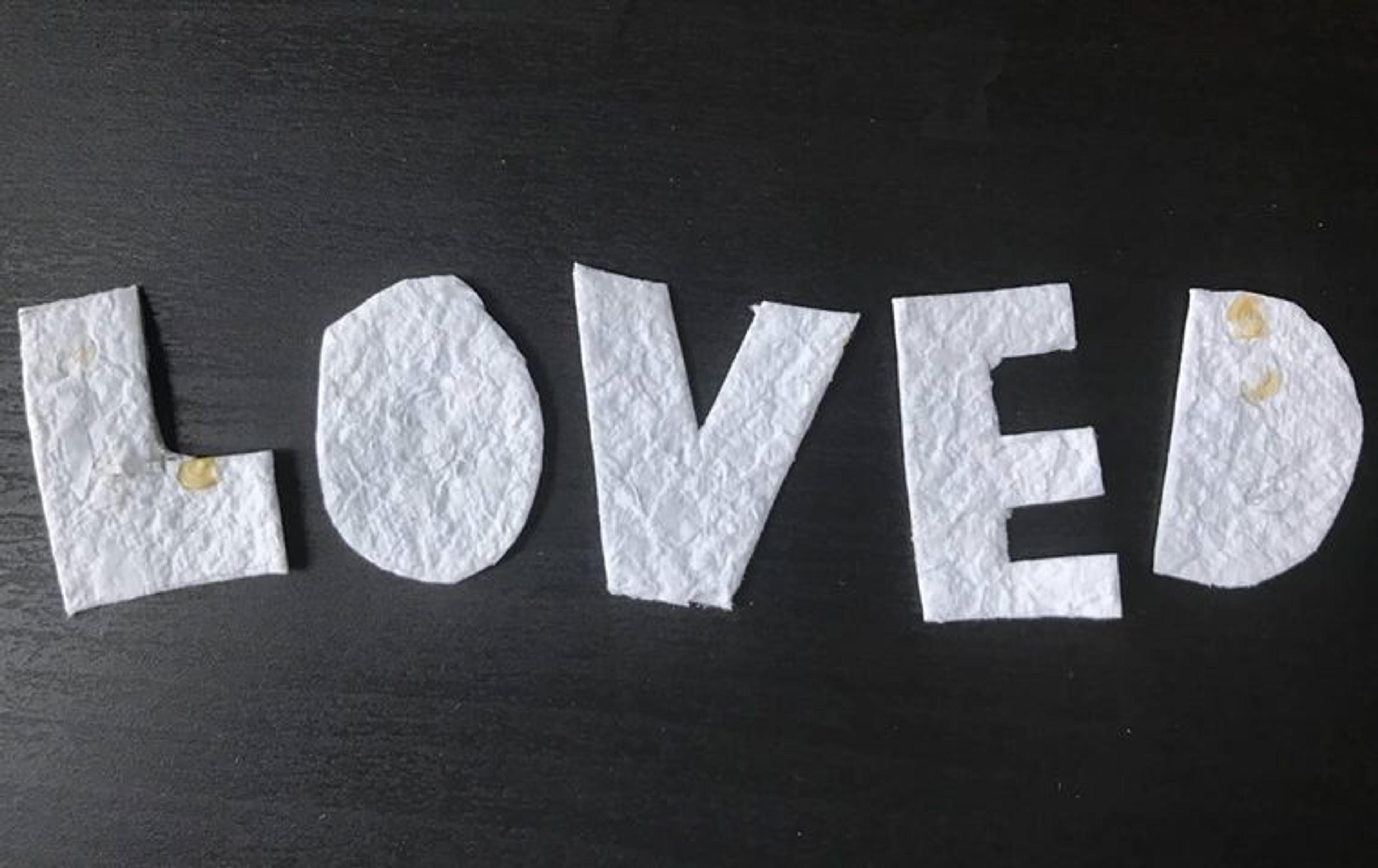 The word "LOVED" cut out of hand-made, seeded paper