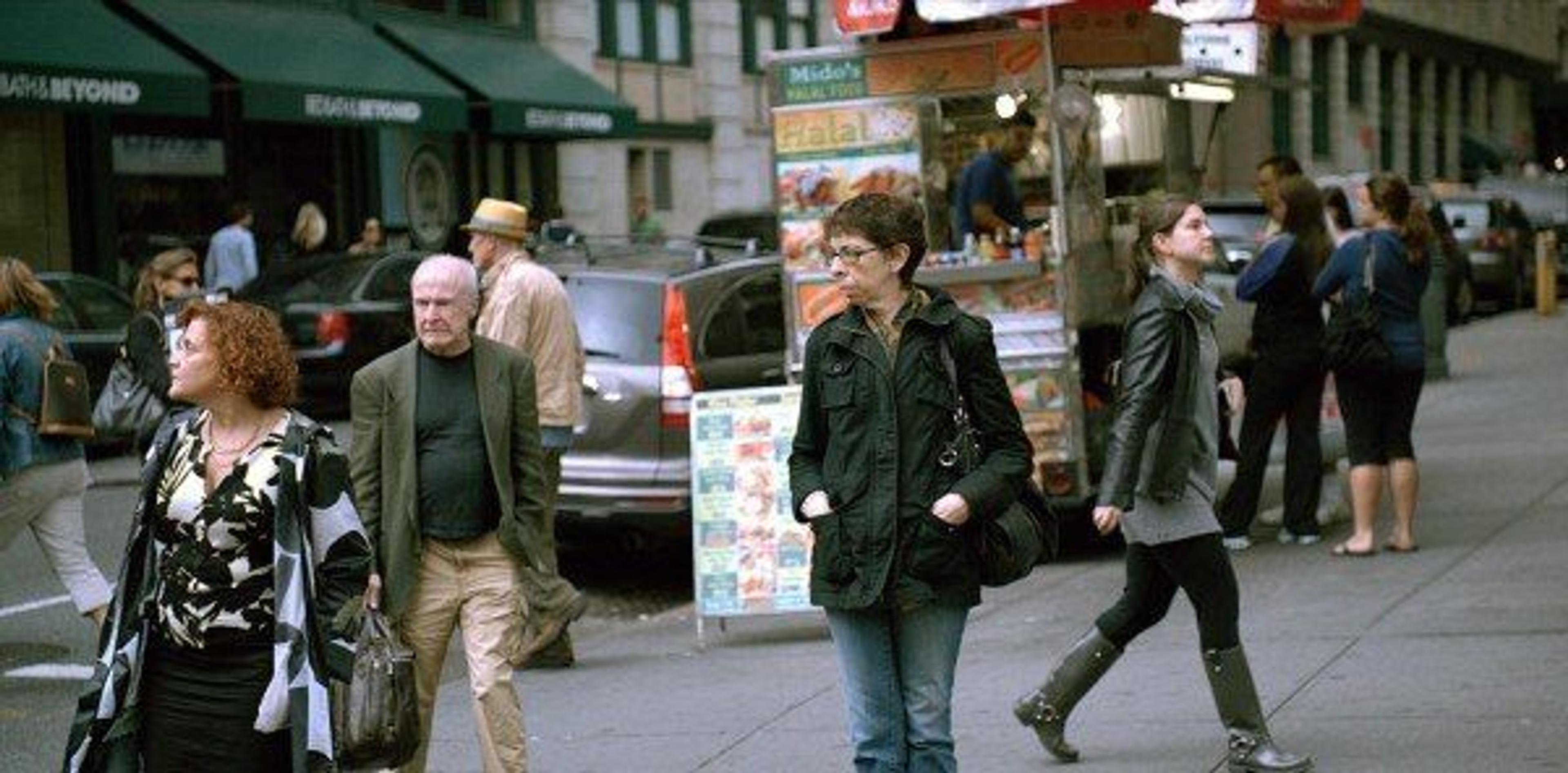 A color video still of a busy urban street with people walking in all different directions