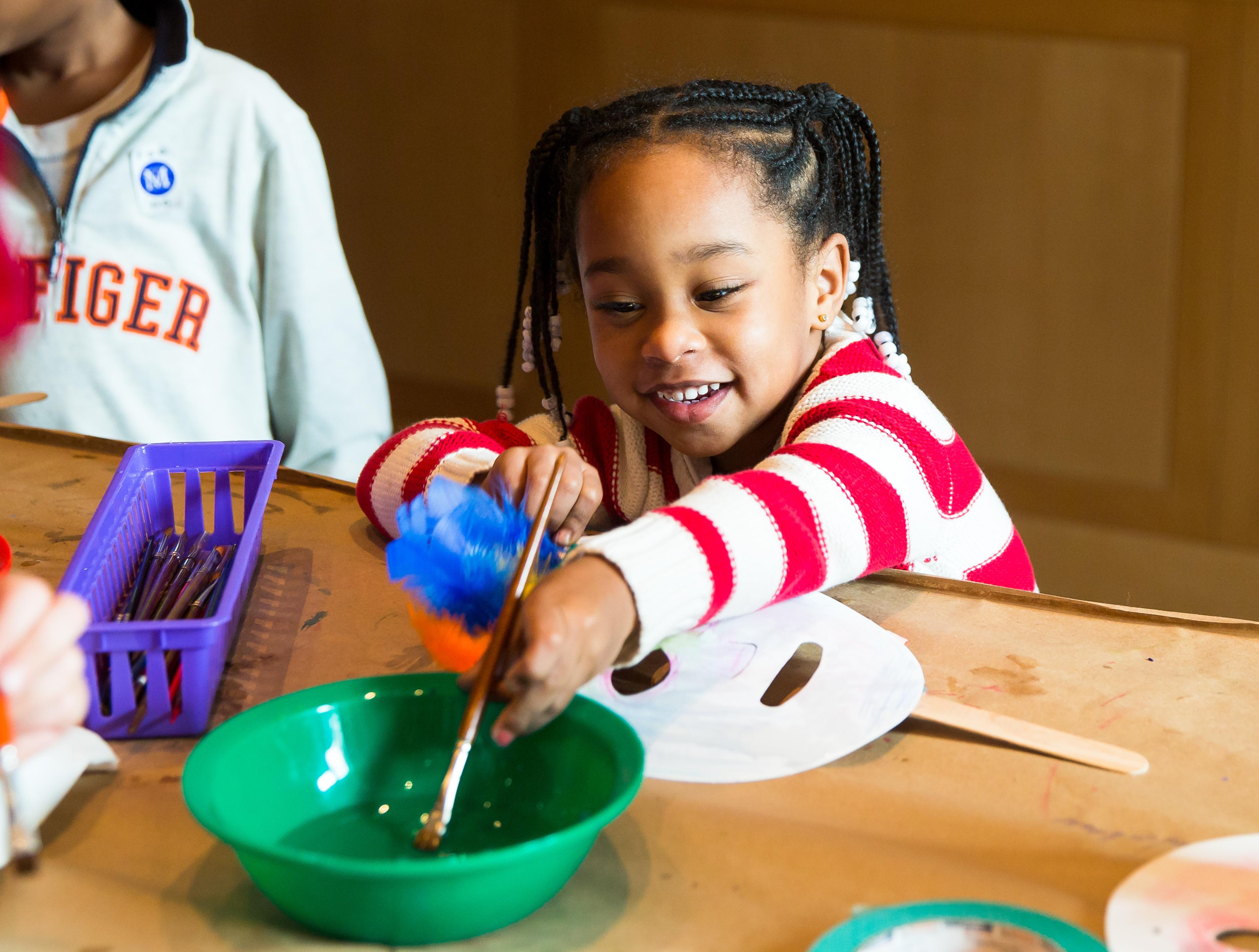 A young Black girl smiles as she participates in an art making activitiy.