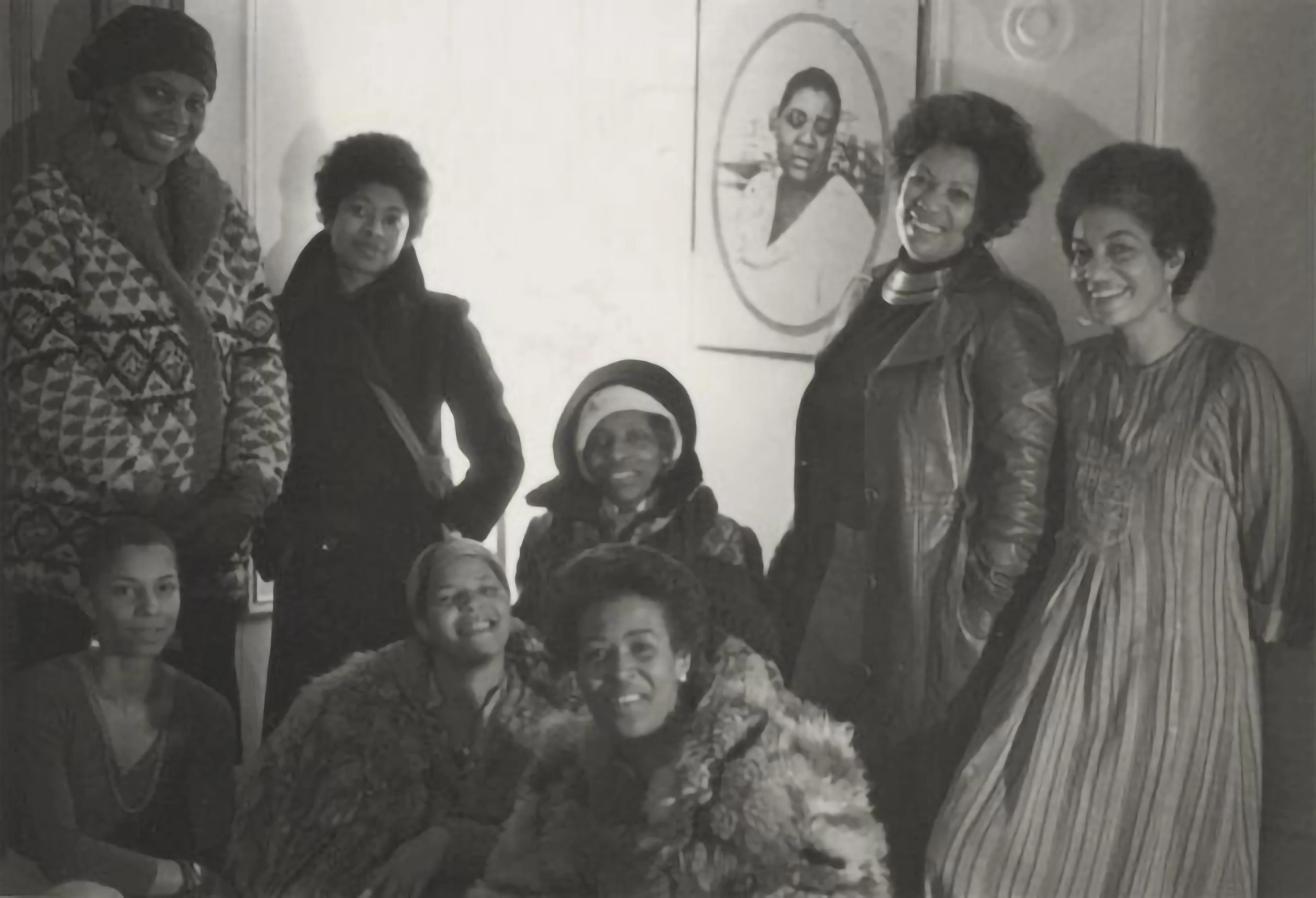 Black-and-white archival photograph of eight Black women literary figures, posed casually against a light-colored wall.