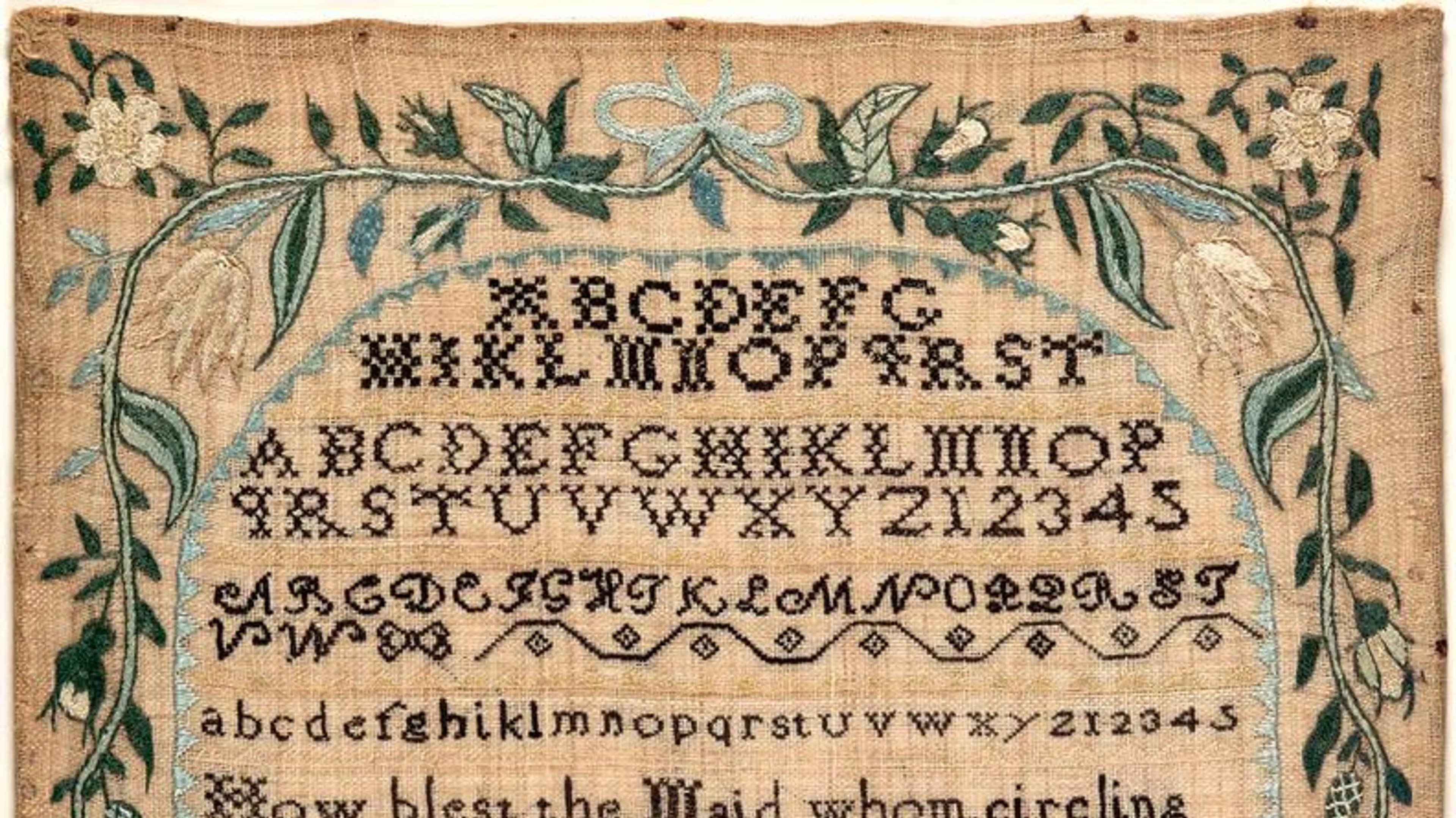 Partial image of a sampler by Lydia Pearson. The design features the alphabet embroidered in black, surrounded by a border of blue, green, and cream-colored flowers, plants, and shapes.