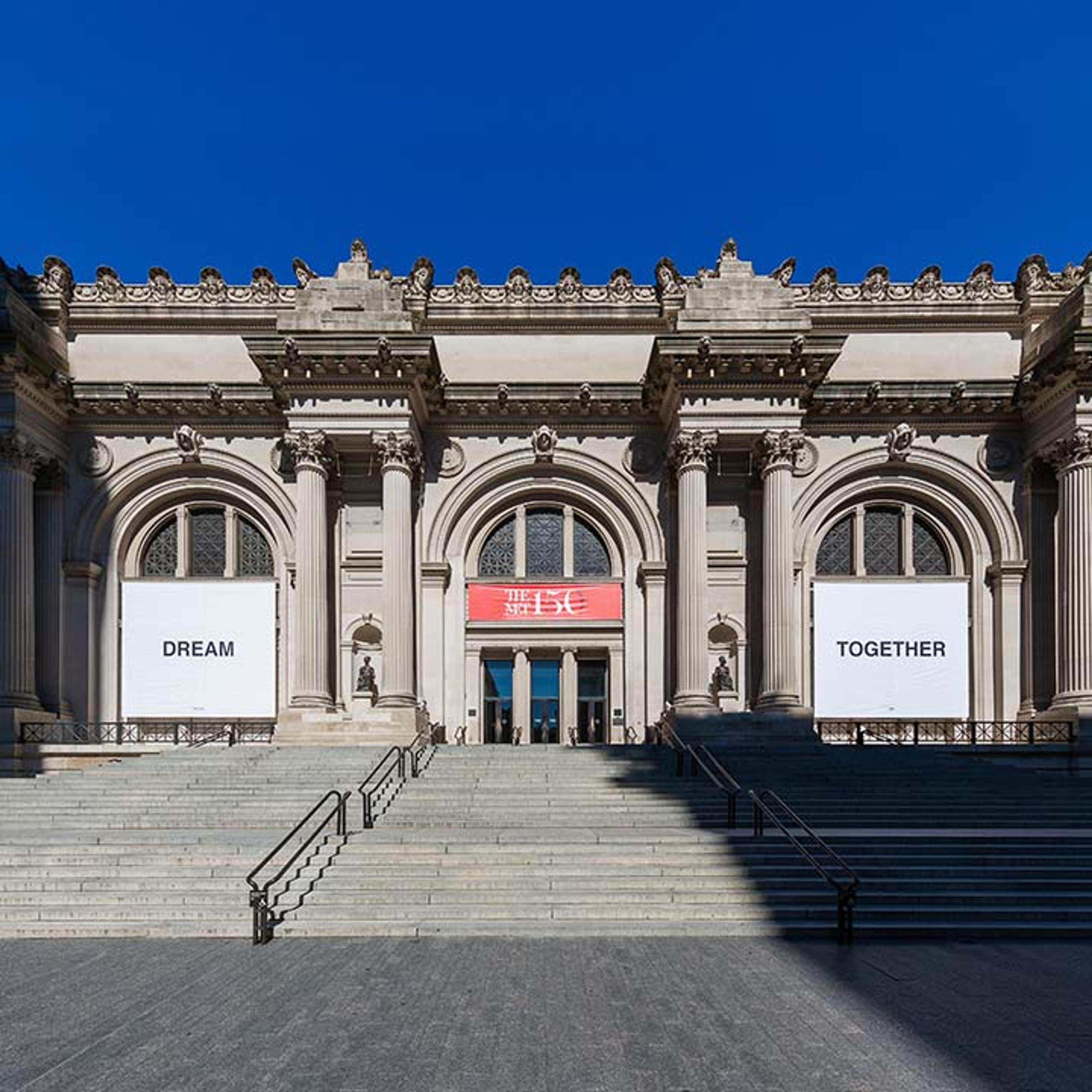 The Met Fifth Avenue facade with two banners by Yoko Ono flanking the entrance; on left "DREAM", on right "TOGETHER", with black text on white ground.
