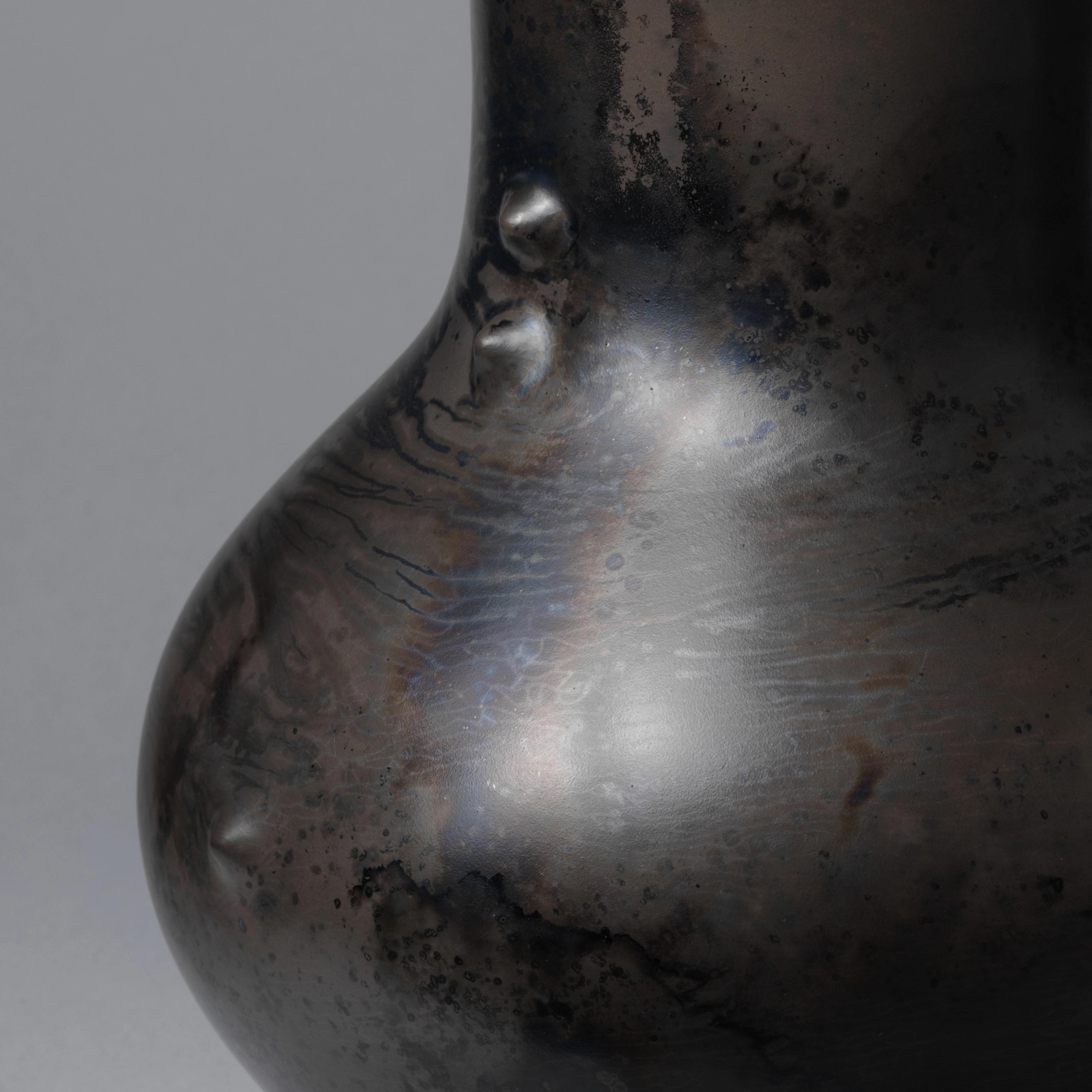 Detail of a black ceramic vessel with a shiny, burnished surface and two small raised bumps at the base of the neck.