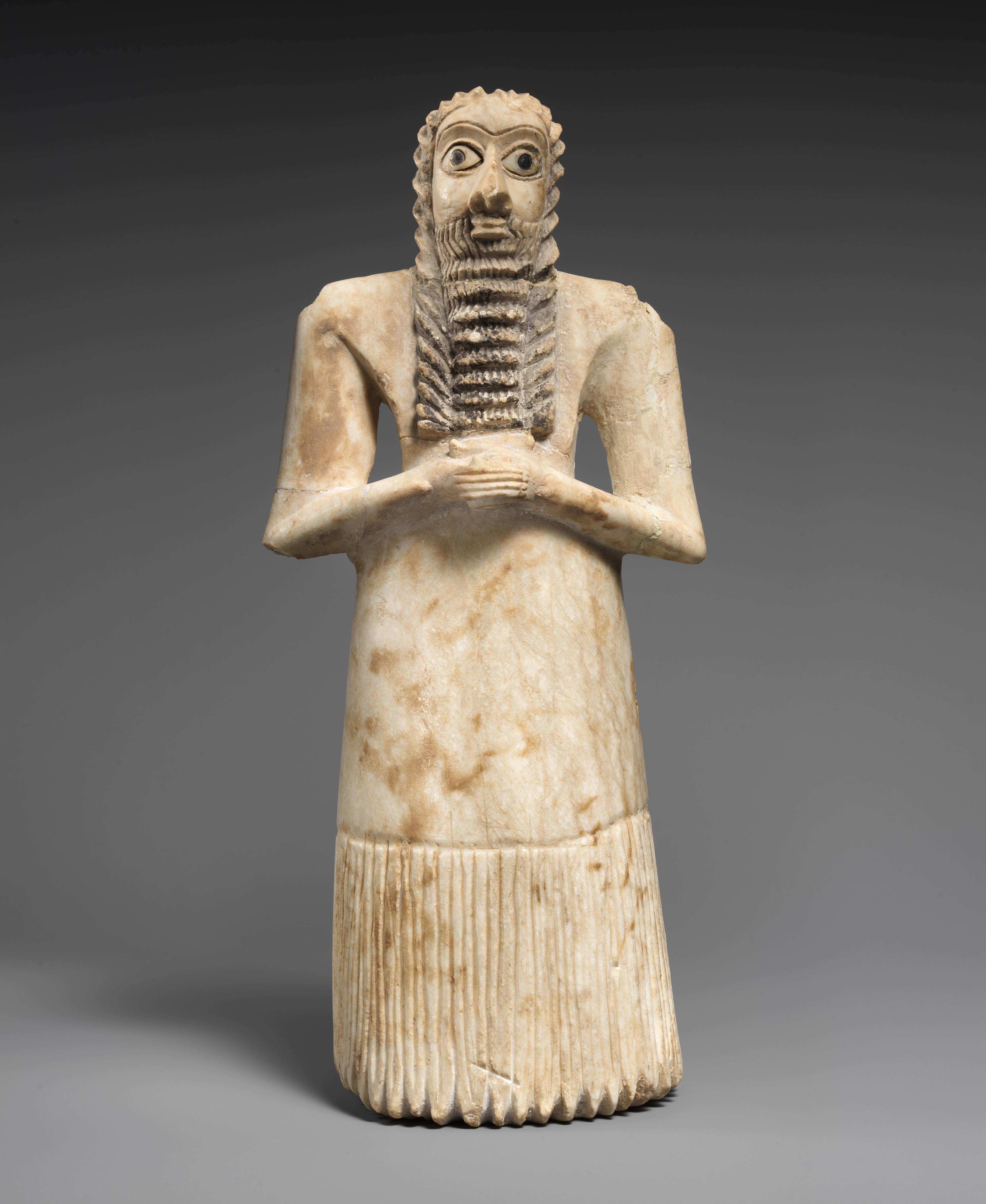 White stone figure with wide eyes and a long, ridged beard, clasping his hands across his chest.