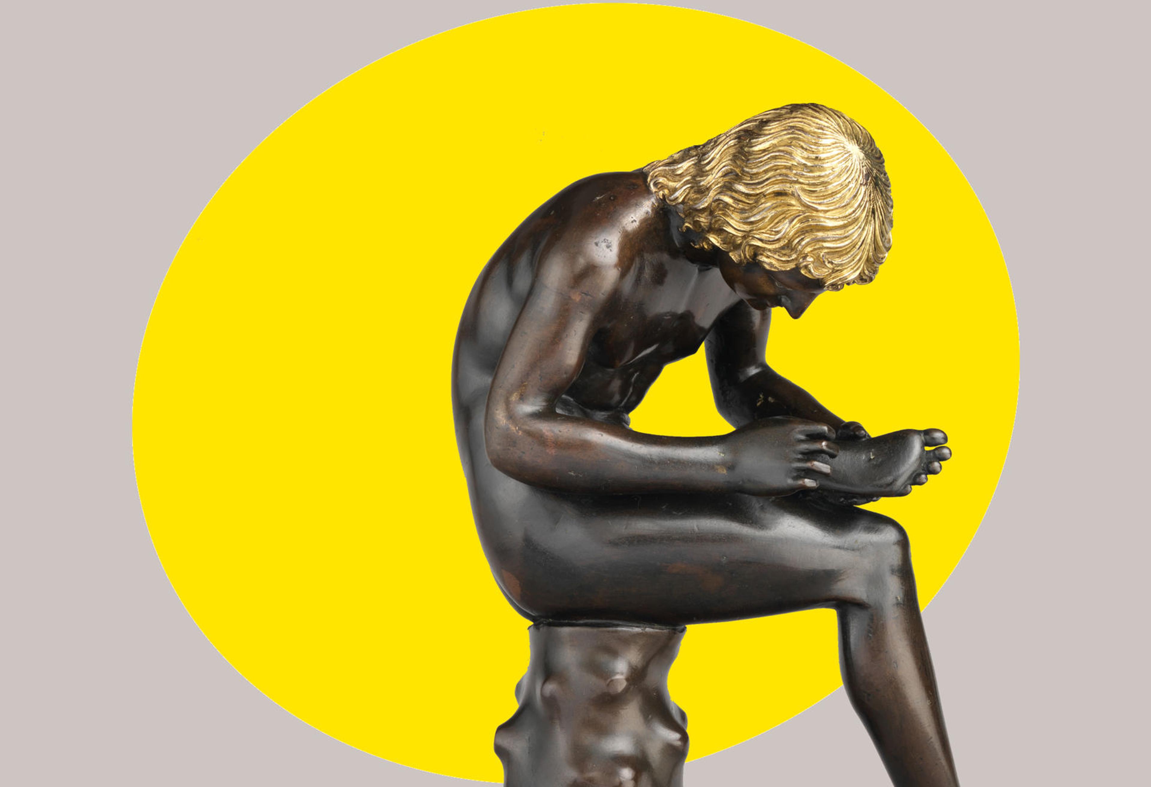 A small bronze sculpture of a seated boy pulling a thorn from the bottom of his foot appears set against a bright yellow ovular spotlight shape in the background.