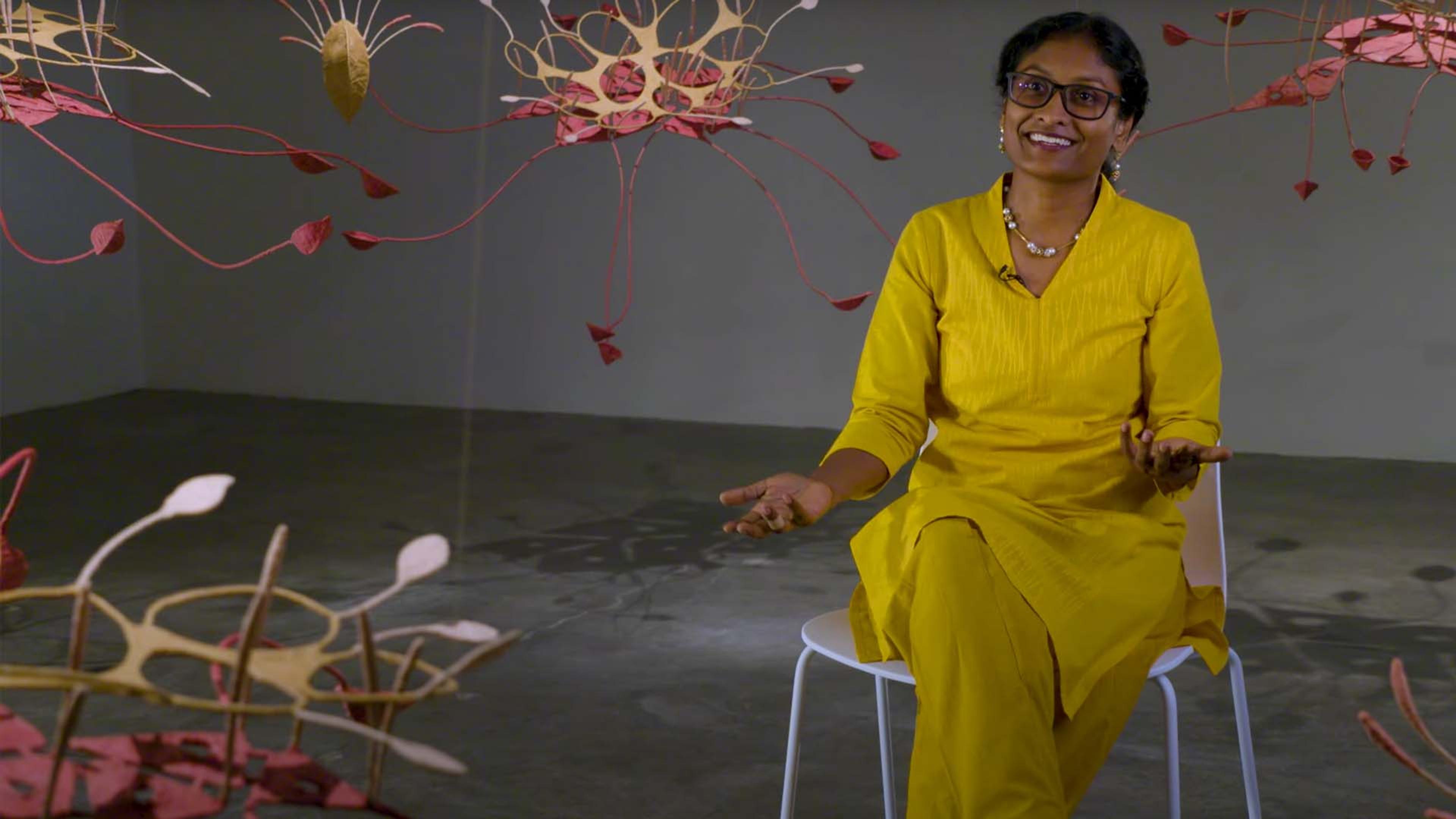Woman in yellow dress sitting in grey room with red colored installations