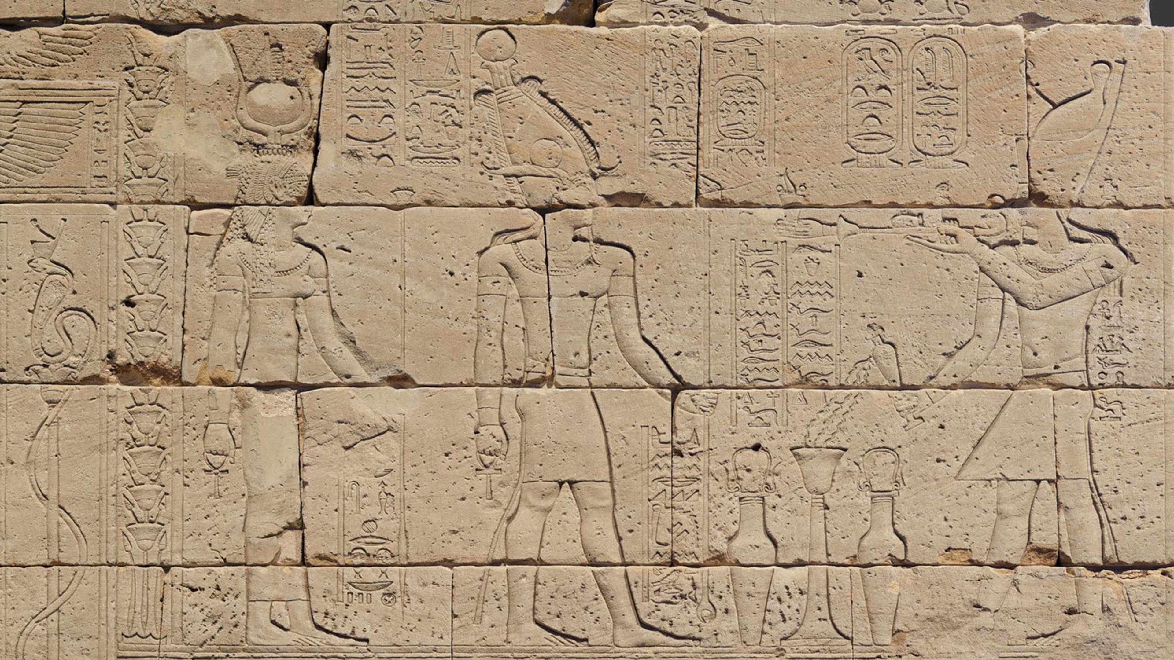 Detail of temple wall depicting Augustus (right) burning incense and pouring milk for the god Osiris (center) and the goddess Isis (left).