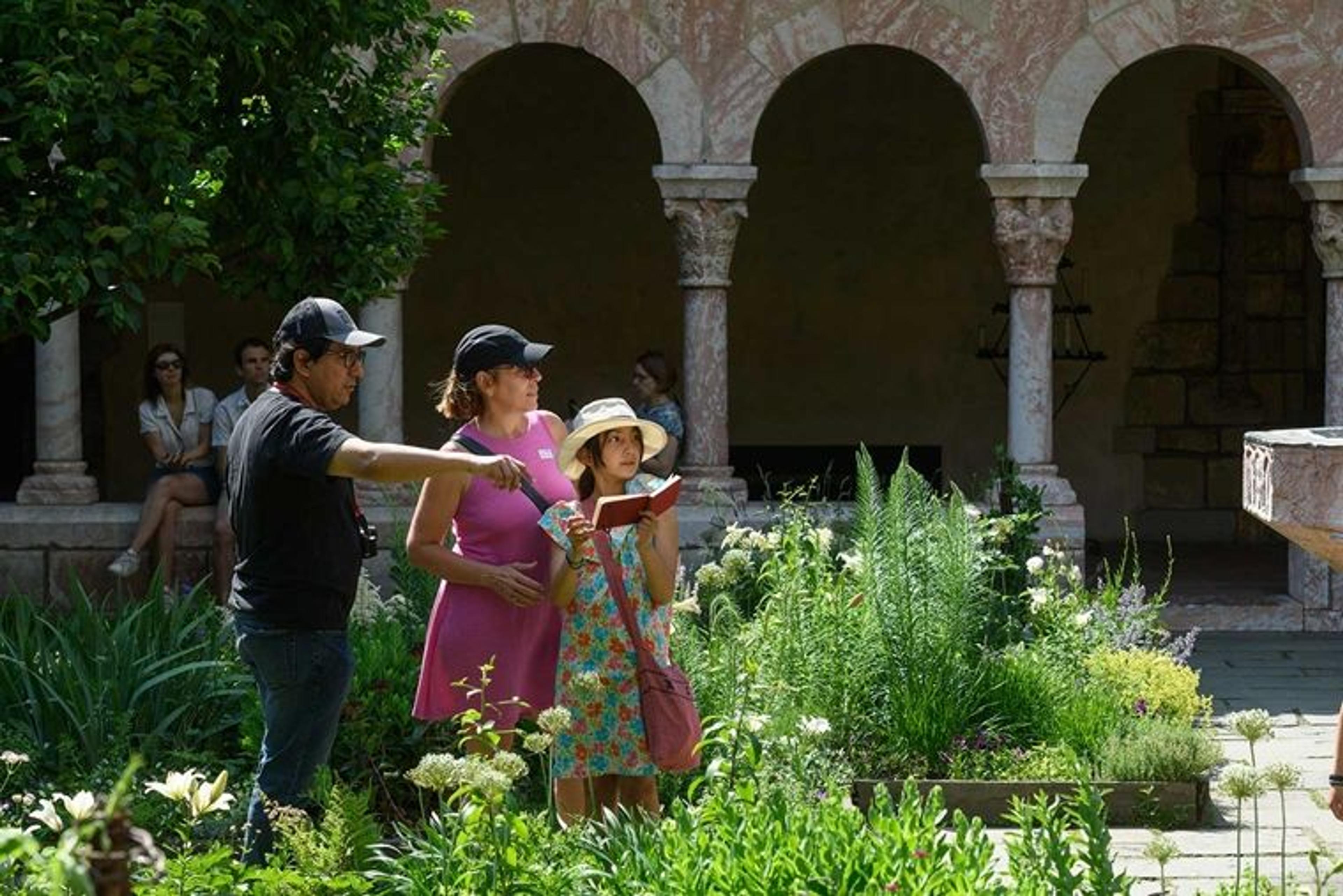 A daughter, father, and mother enjoying a sunny day among garden beds in a medieval cloister.