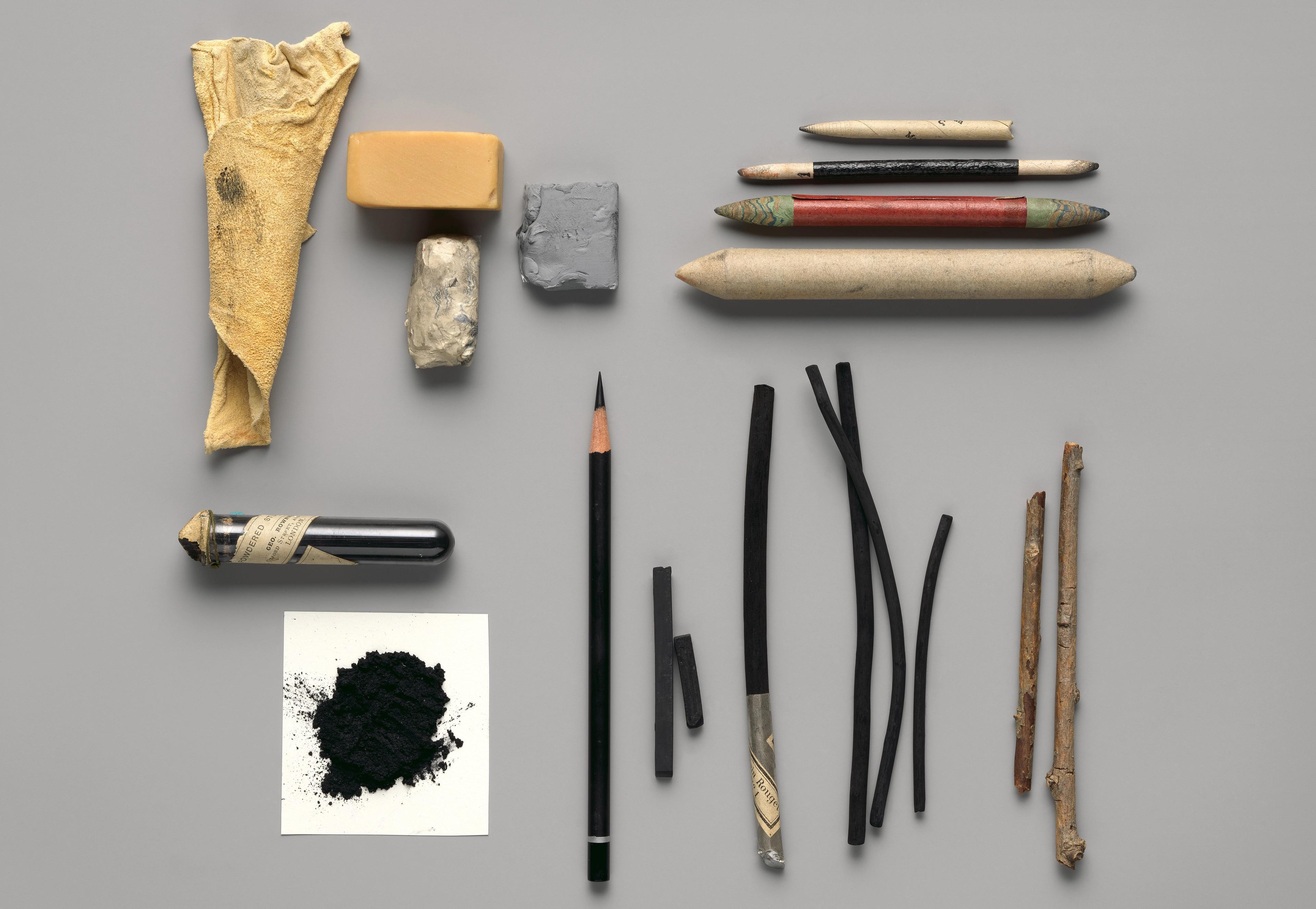 An artful arrangement of pencils, charcoal sticks, erasers, twigs, and other tools for charcoal drawing.