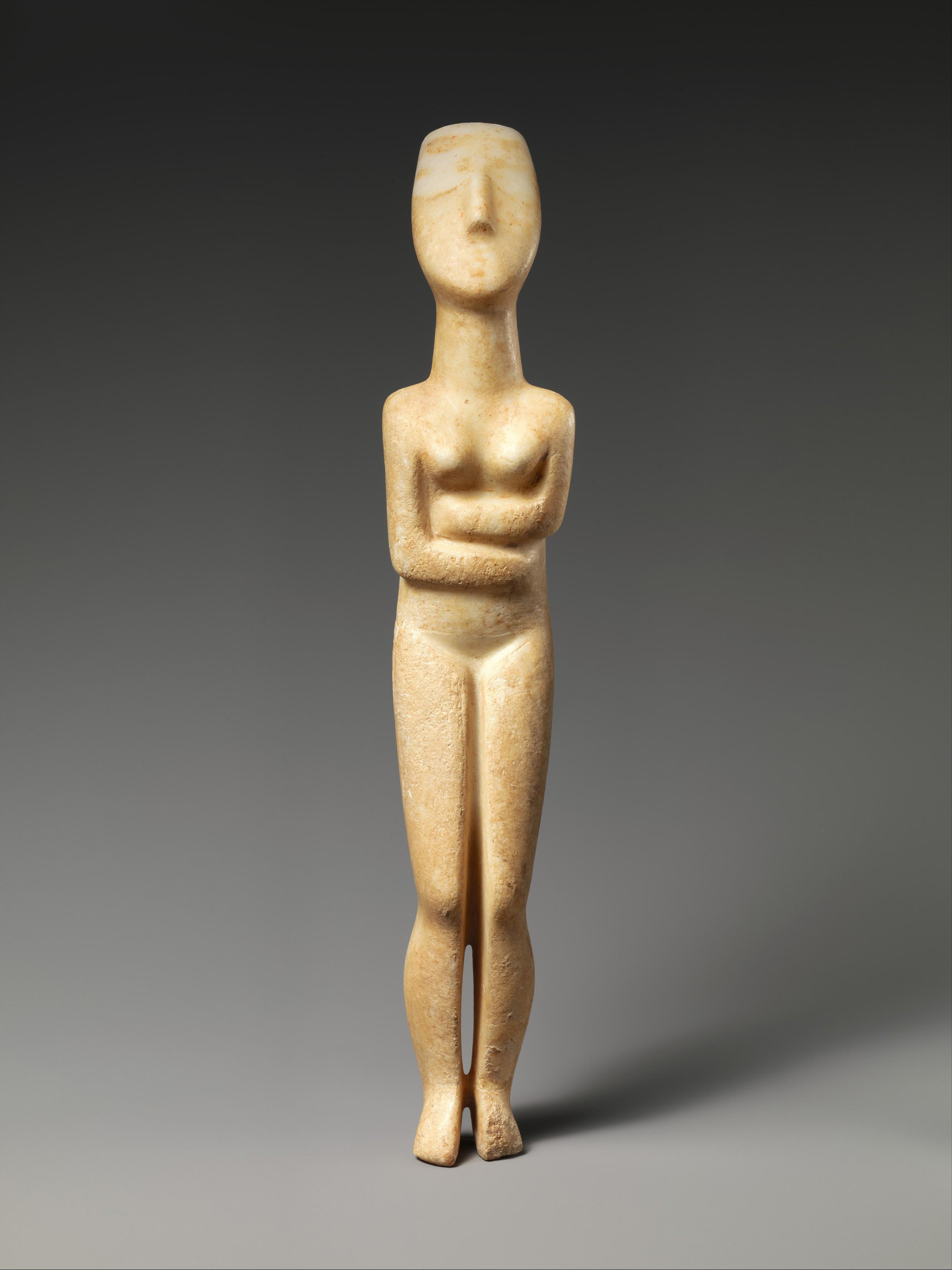 Marble figurine of a standing woman with folded arms and simplified features against a gray background.