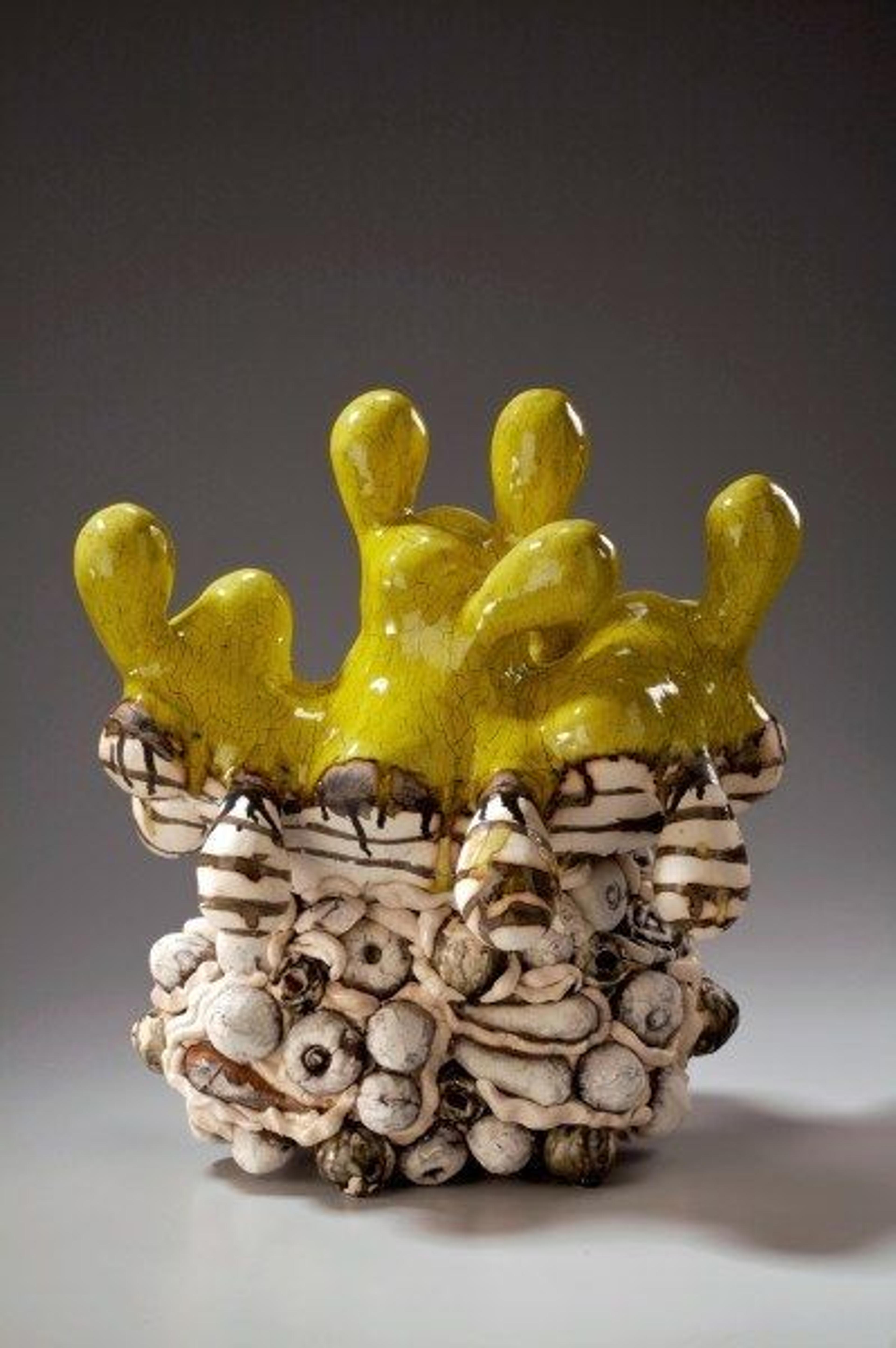 A small ceramics piece with yellow fingerlike forms emerging from a cream and brown bumpy vessel